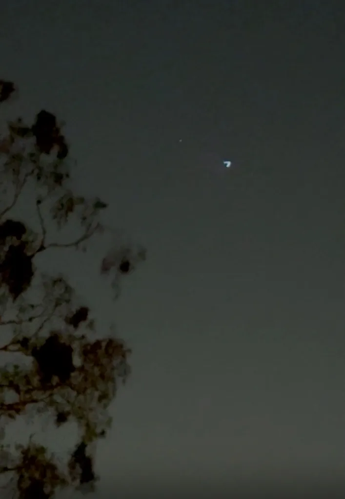 A chevron-shaped object with a white light, possibly a kite, in the night sky.