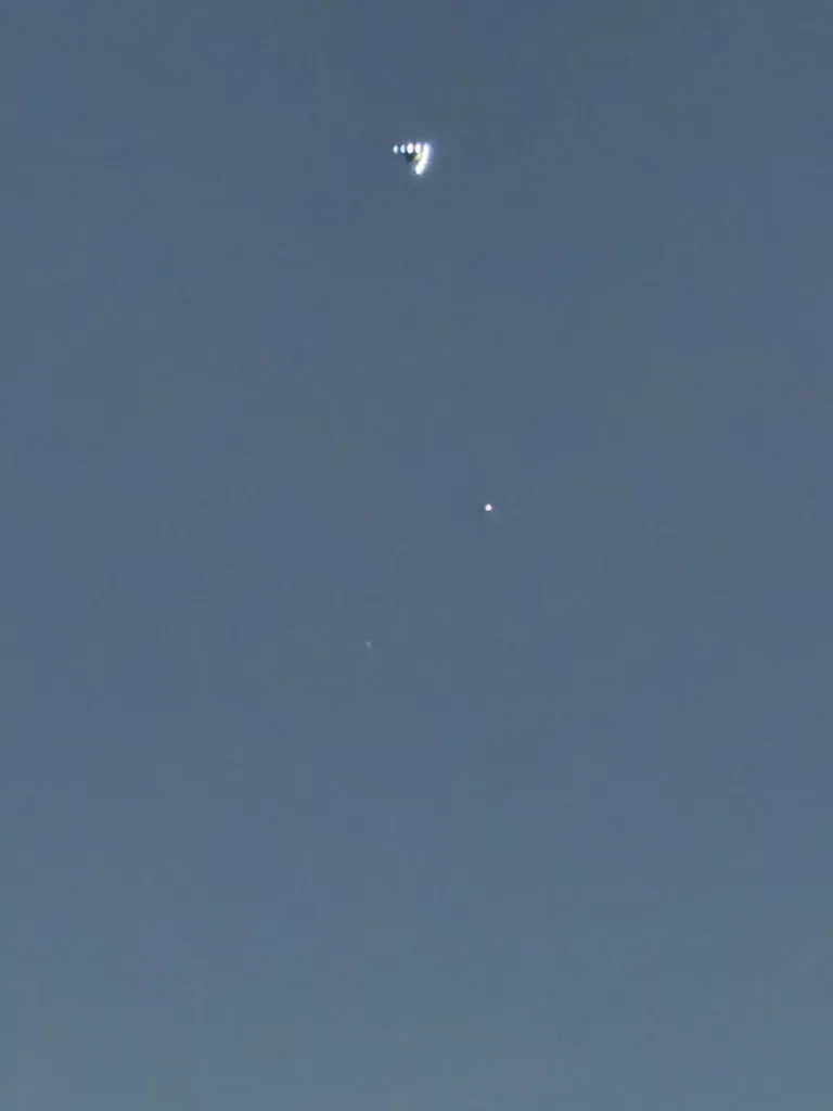 Photograph of a chevron-shaped craft with white lights in a blue sky.