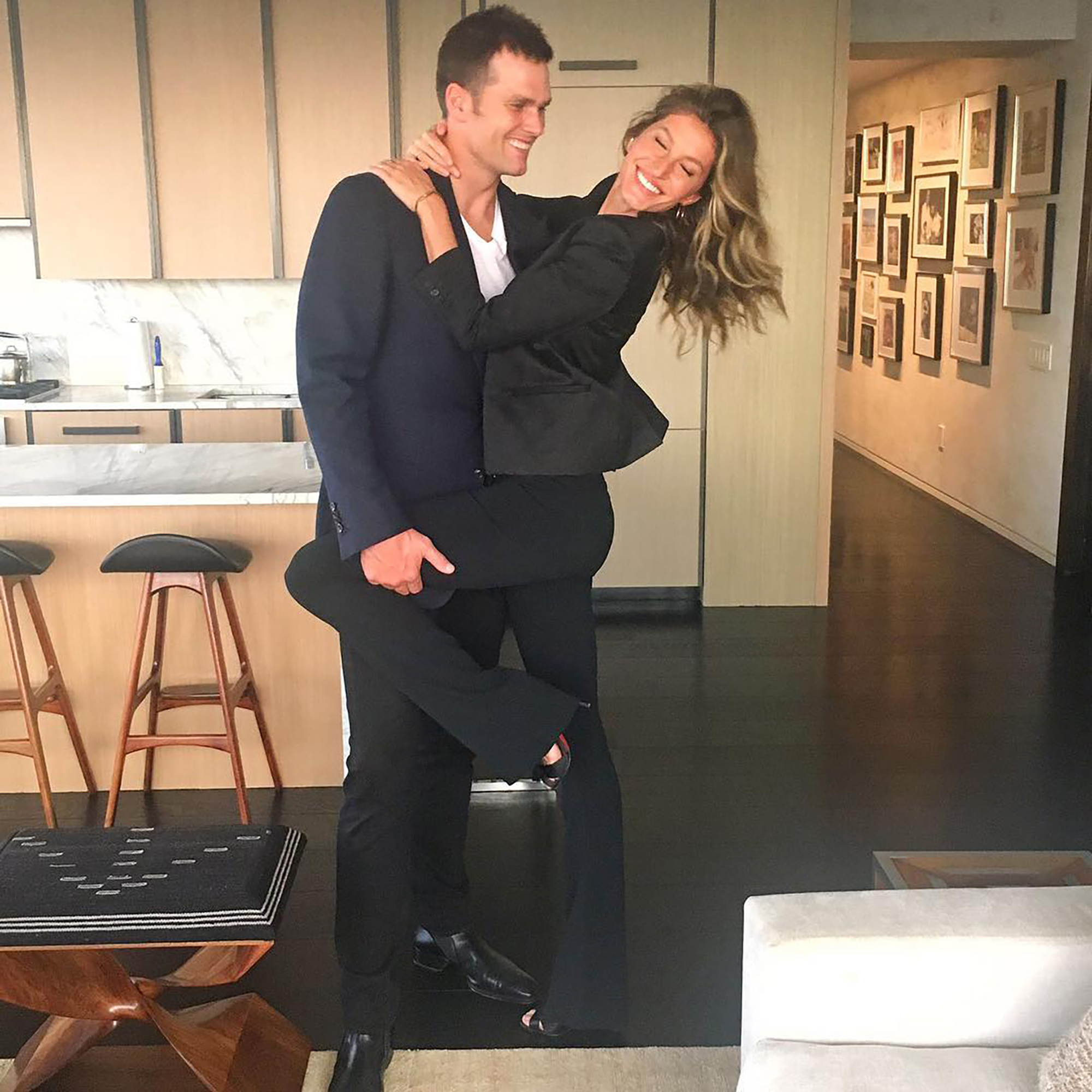 Tom Brady holding Gisele Bündchen in his arms in a kitchen.