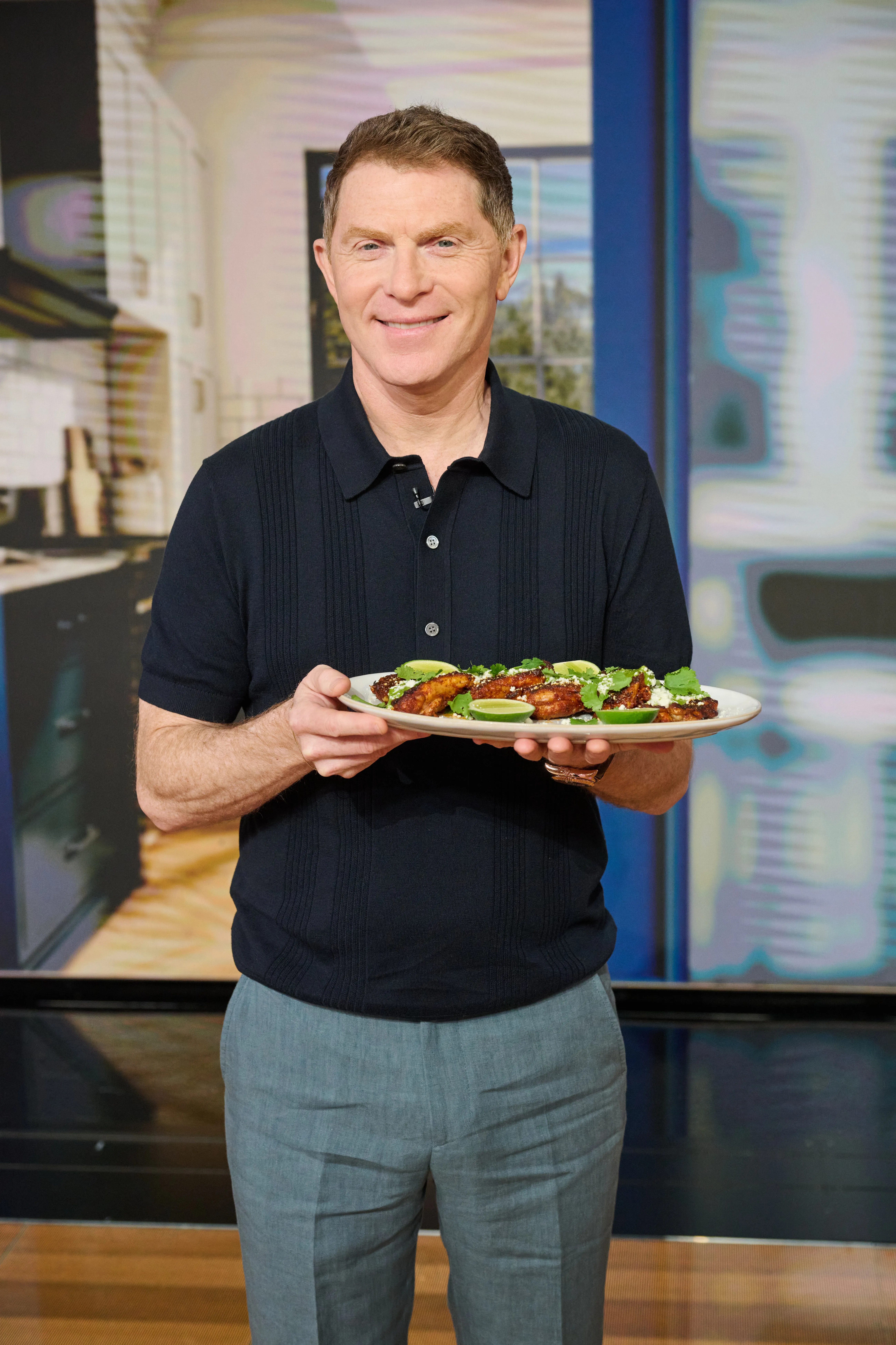Bobby Flay holding a plate of food garnished with cilantro and lime wedges.