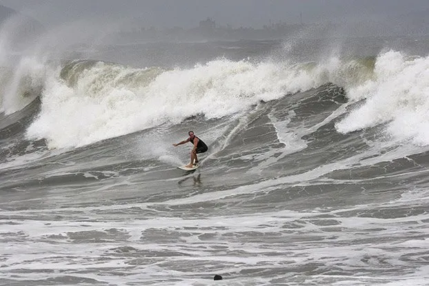 A male surfer in a black wetsuit rides a large, powerful wave at Ocean Beach, San Francisco.