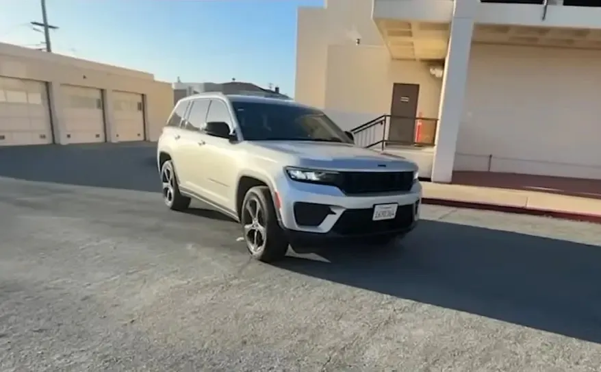 A silver Jeep Grand Cherokee parked in front of a building with garage doors.