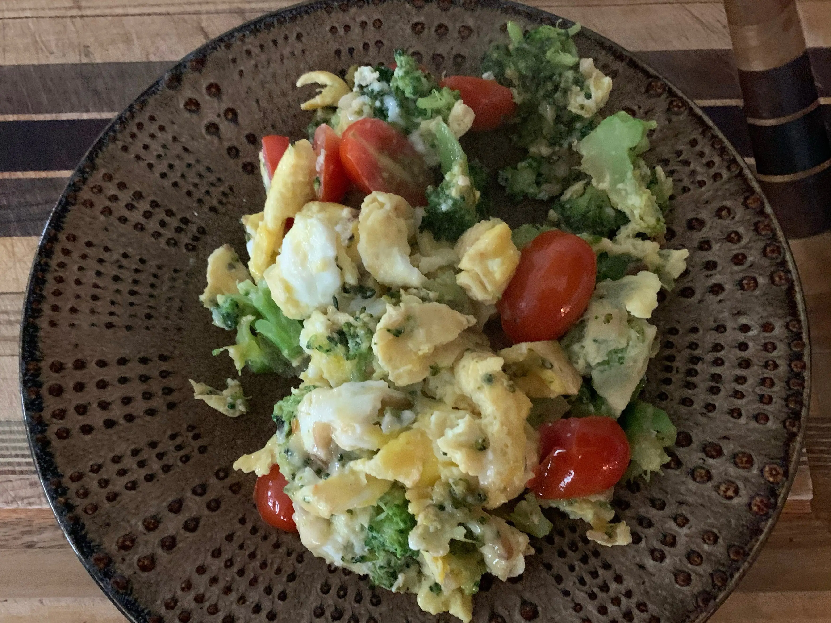 breakfast scramble with broccoli, egg, and tomato on brown plate