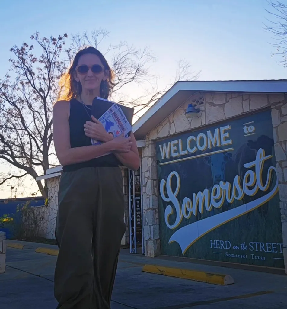 A woman holding campaign flyers for Maureen Galindo stands in front of a 