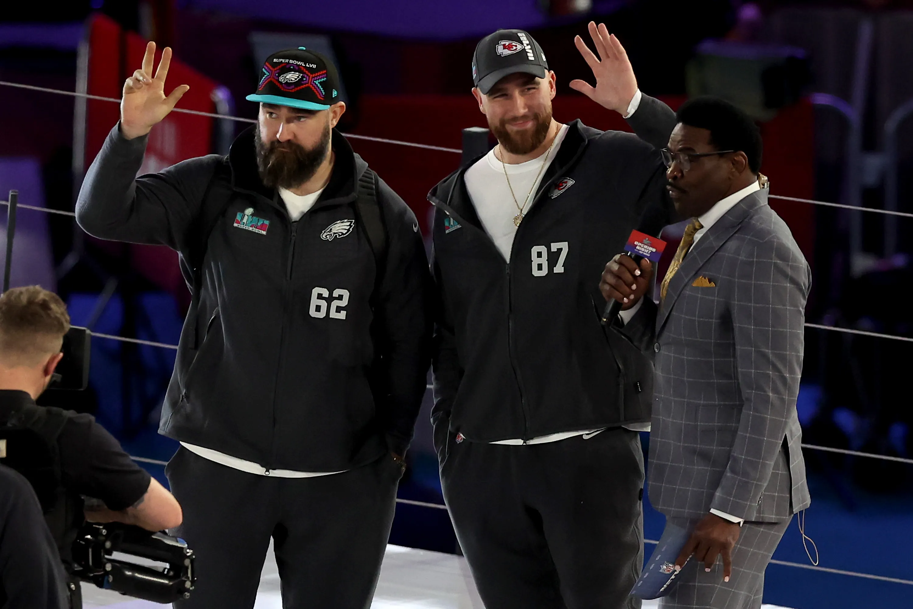 Jason and Travis Kelce wave alongside an interviewer at Super Bowl LVII Opening Night.