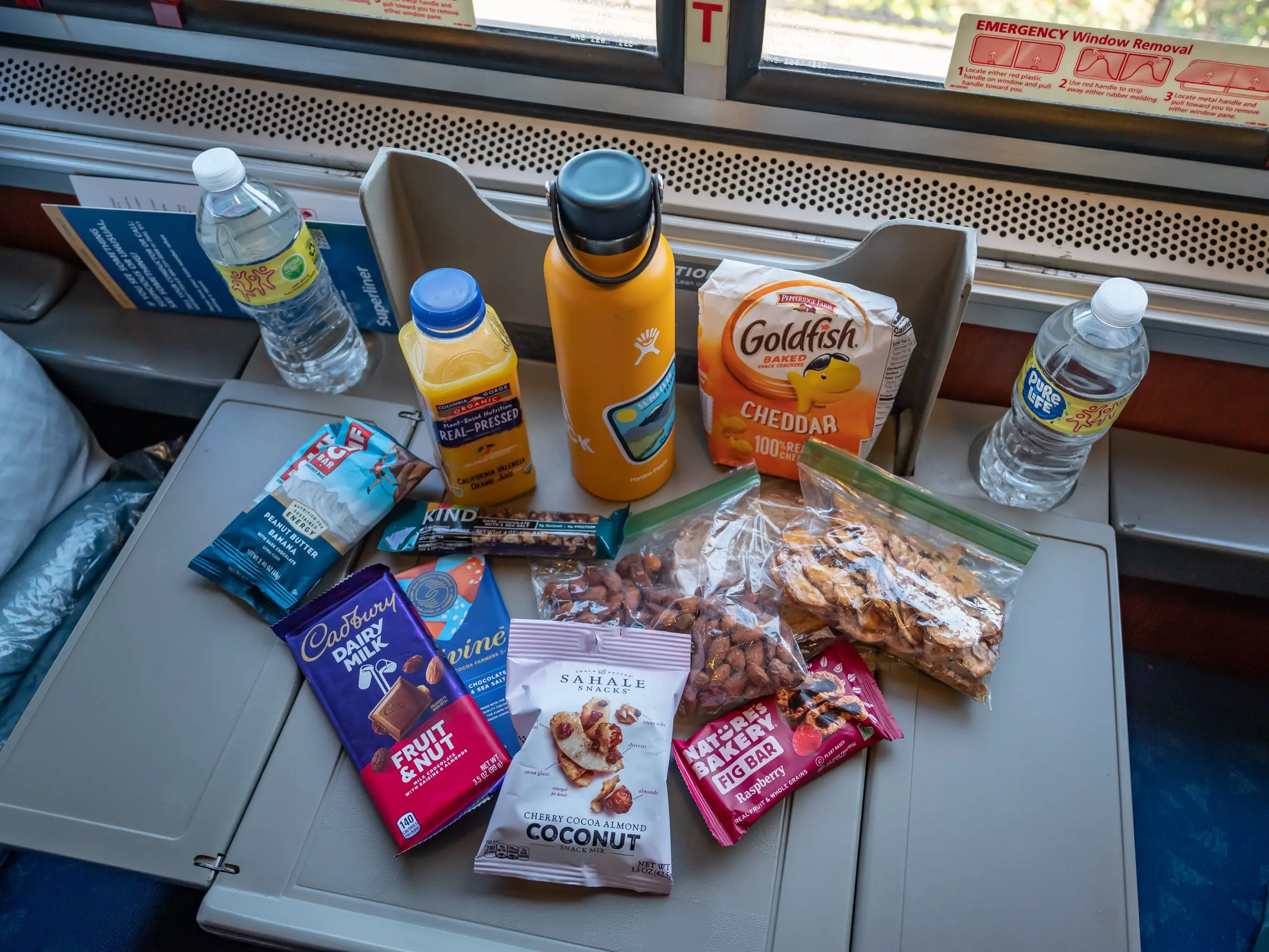 Pull-out tray on Amtrak filled with water bottles, Goldfish crackers, chocolate, granola, pretzels, and other pre-packaged snacks