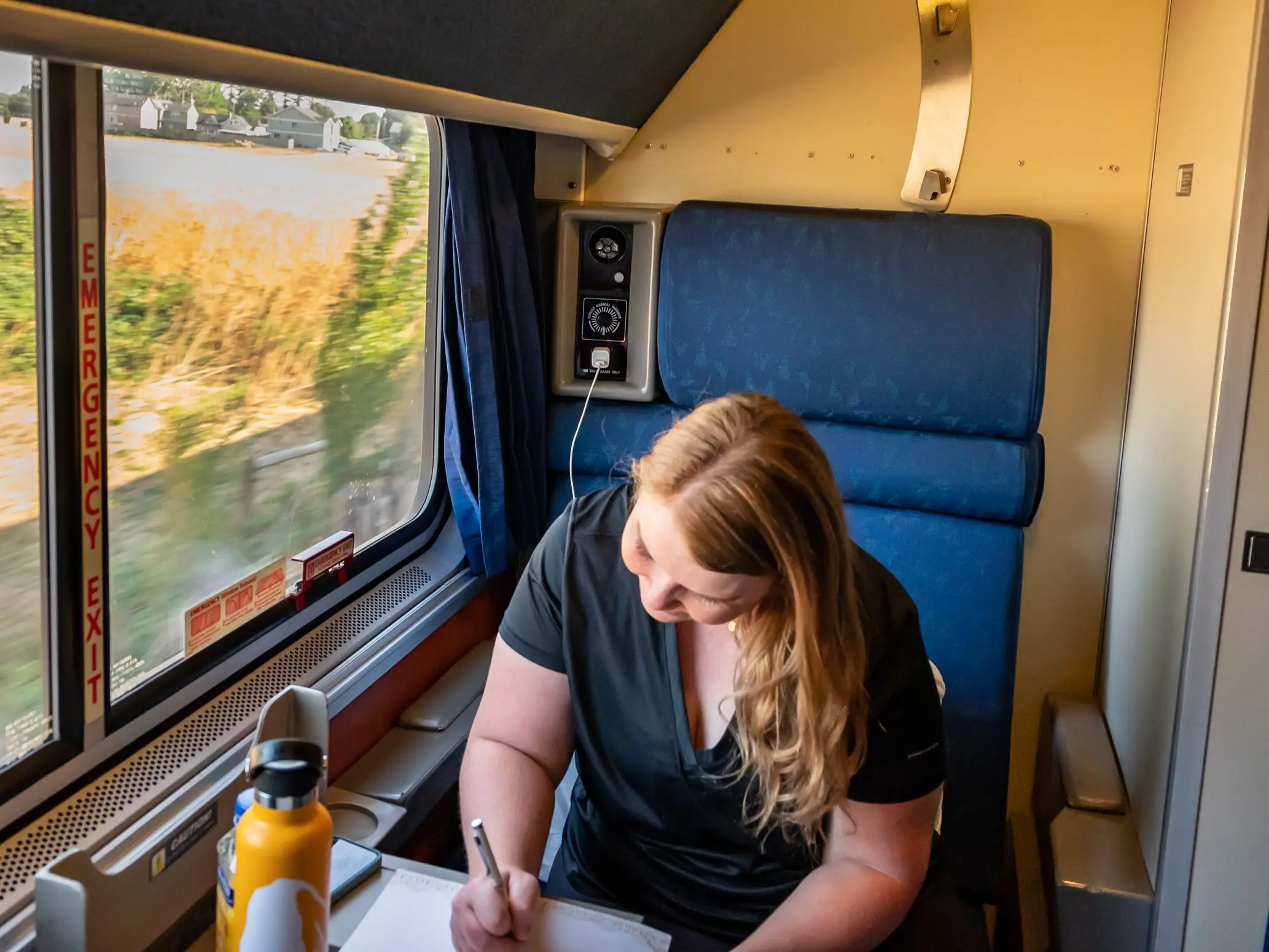 A woman sitting on a train and writing in a journal.