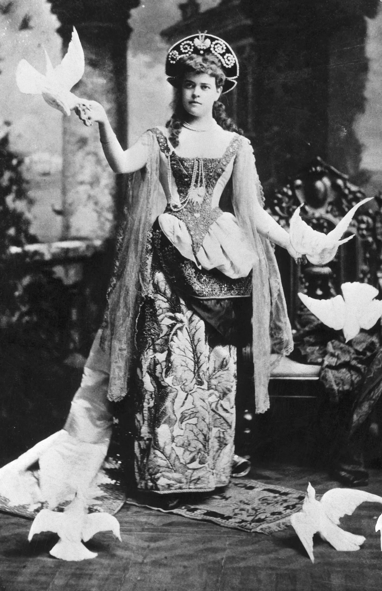 Alva Belmont poses for a portrait with white birds around her, costumed for a fancy dress ball.