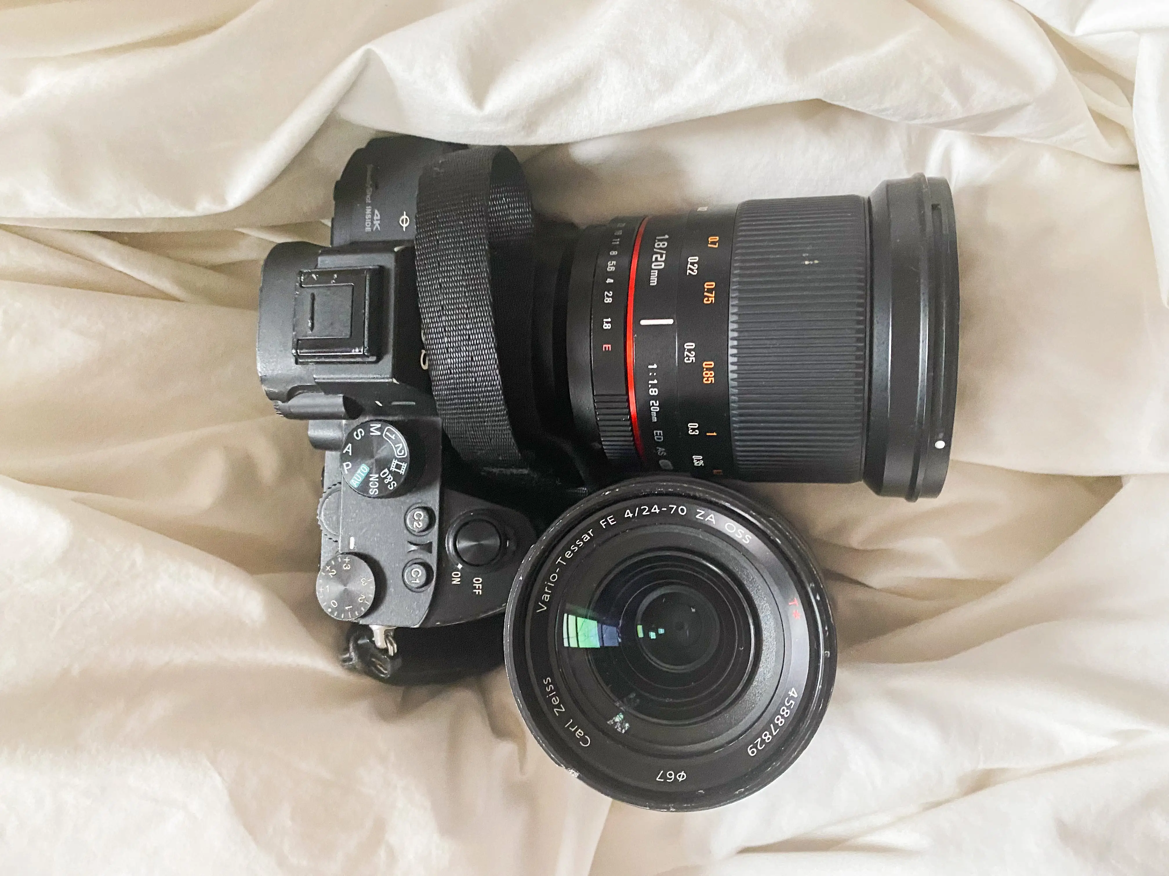 Arial view of a black camera and a detached black lens on a white sheet.