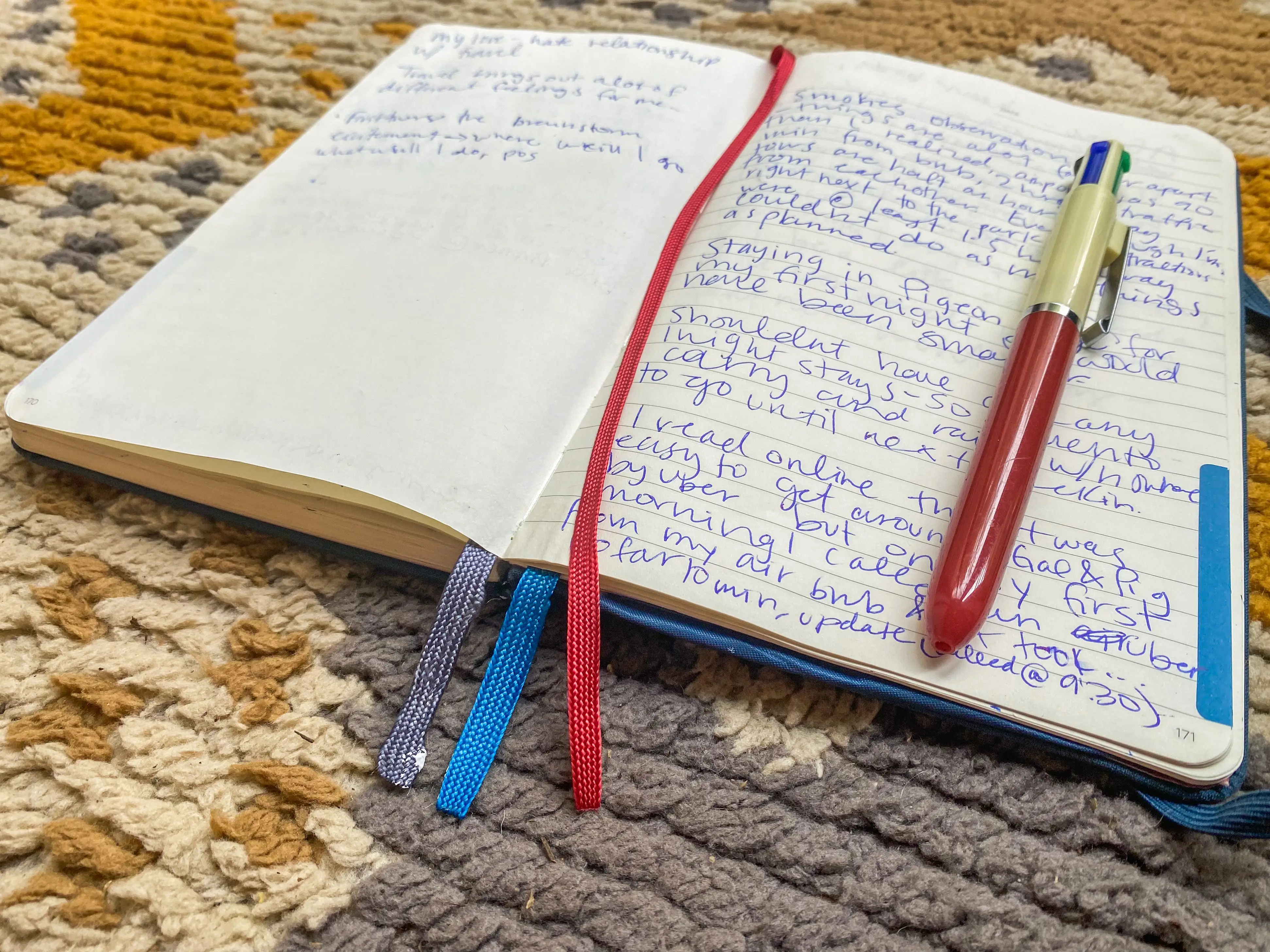 An open notebook with written words, a red book mark, and a red pen on top sits on top of a yellow and gray rug with a geometric pattern