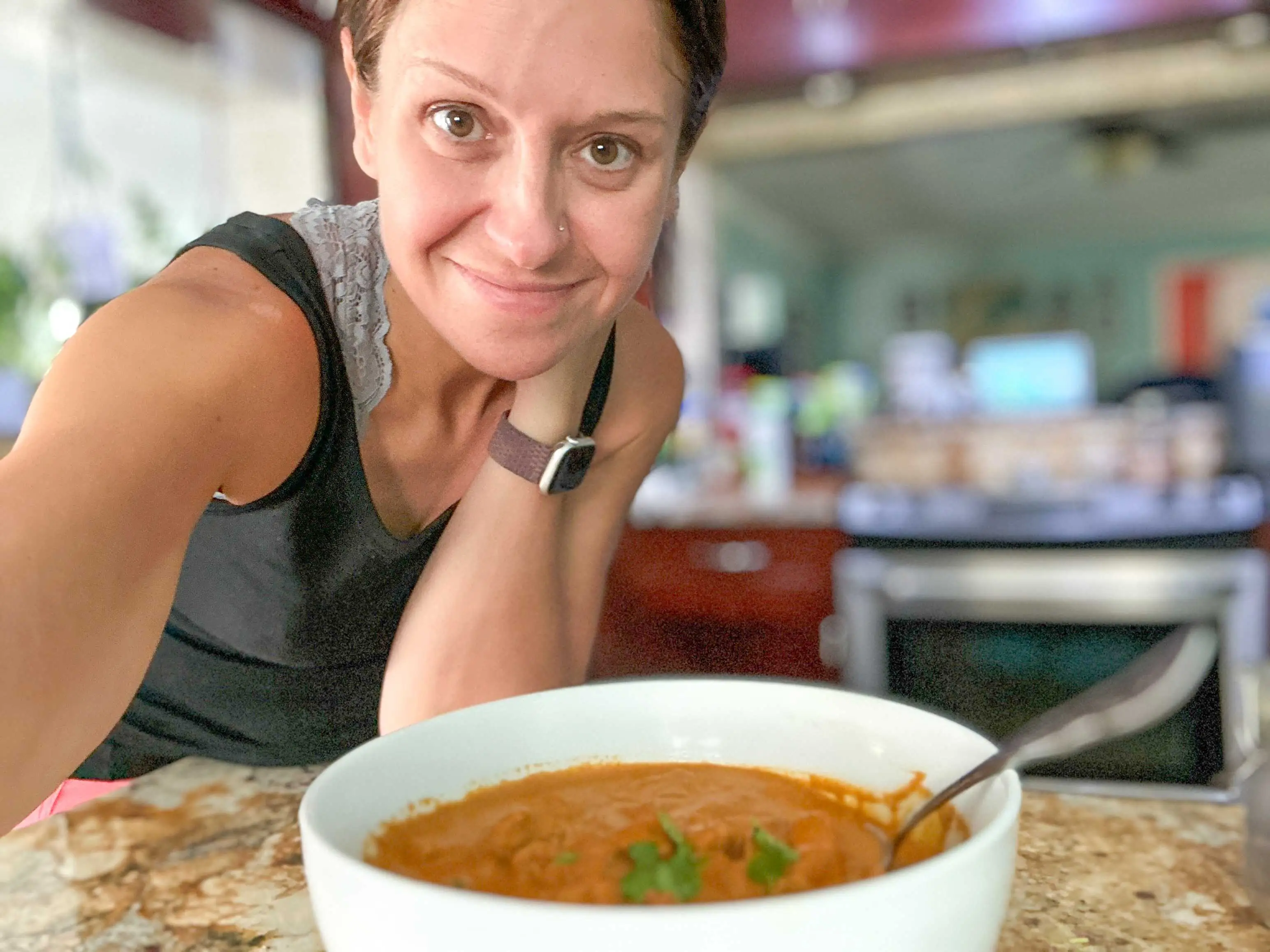Selfie of the writer wearing a black tank top leaning over a kitchen counter with a white bowl of orange chicken curry in front of her