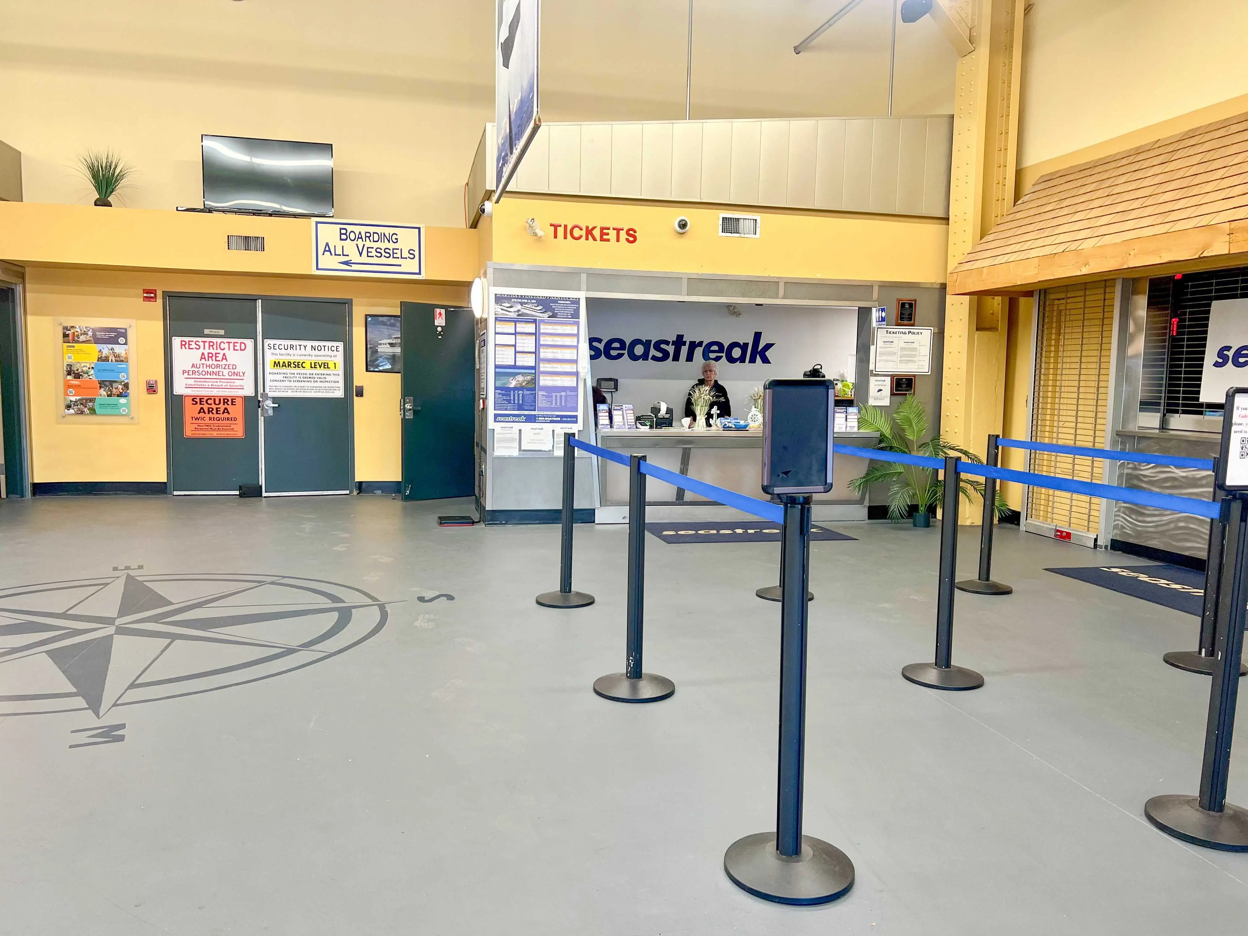 A room with gray floors, yellow walls, and a ticket booth with a worker staffed at the desk. Red lettering above the window says 