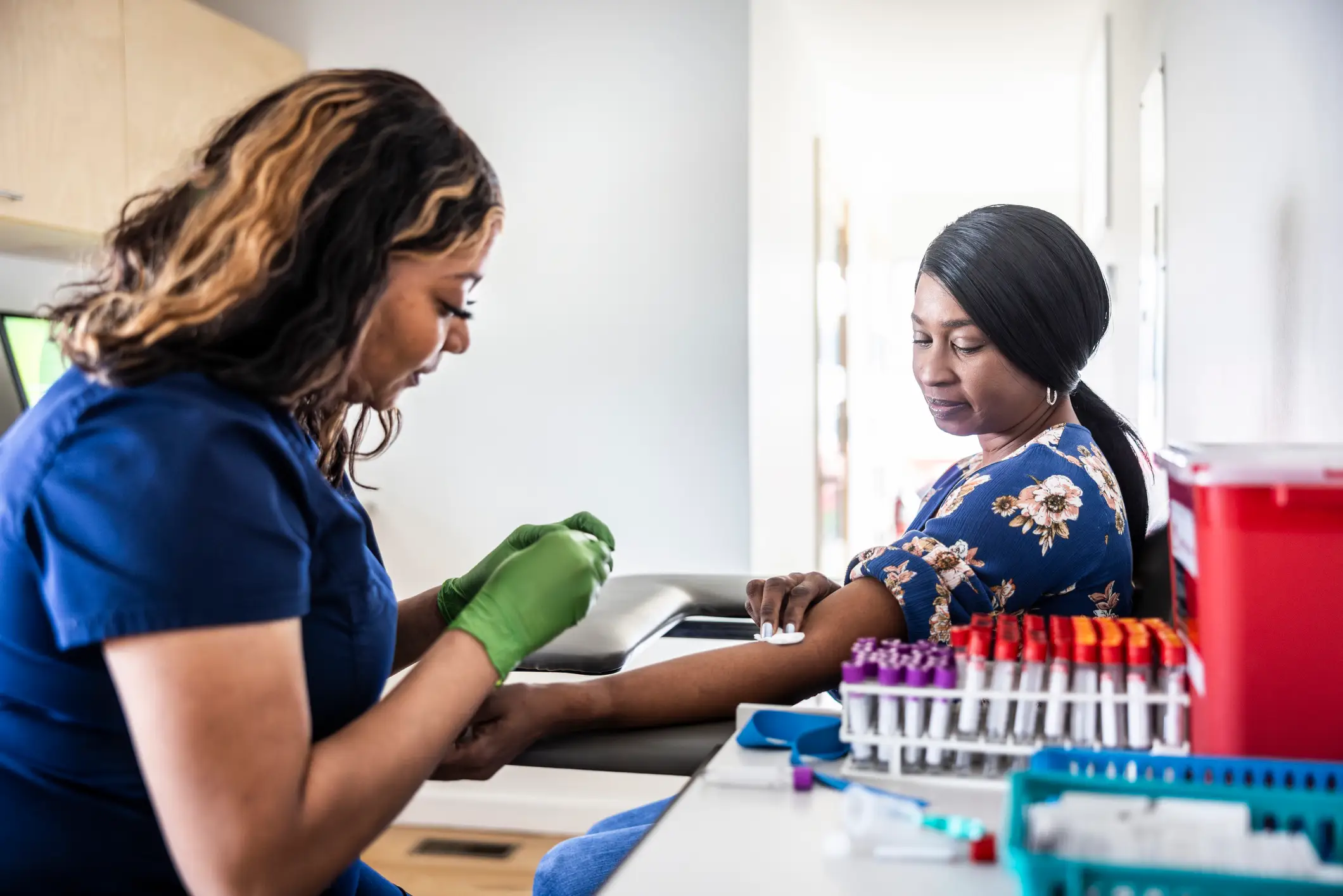 A woman in medical scrubs preparing for a blood draw of a patient.