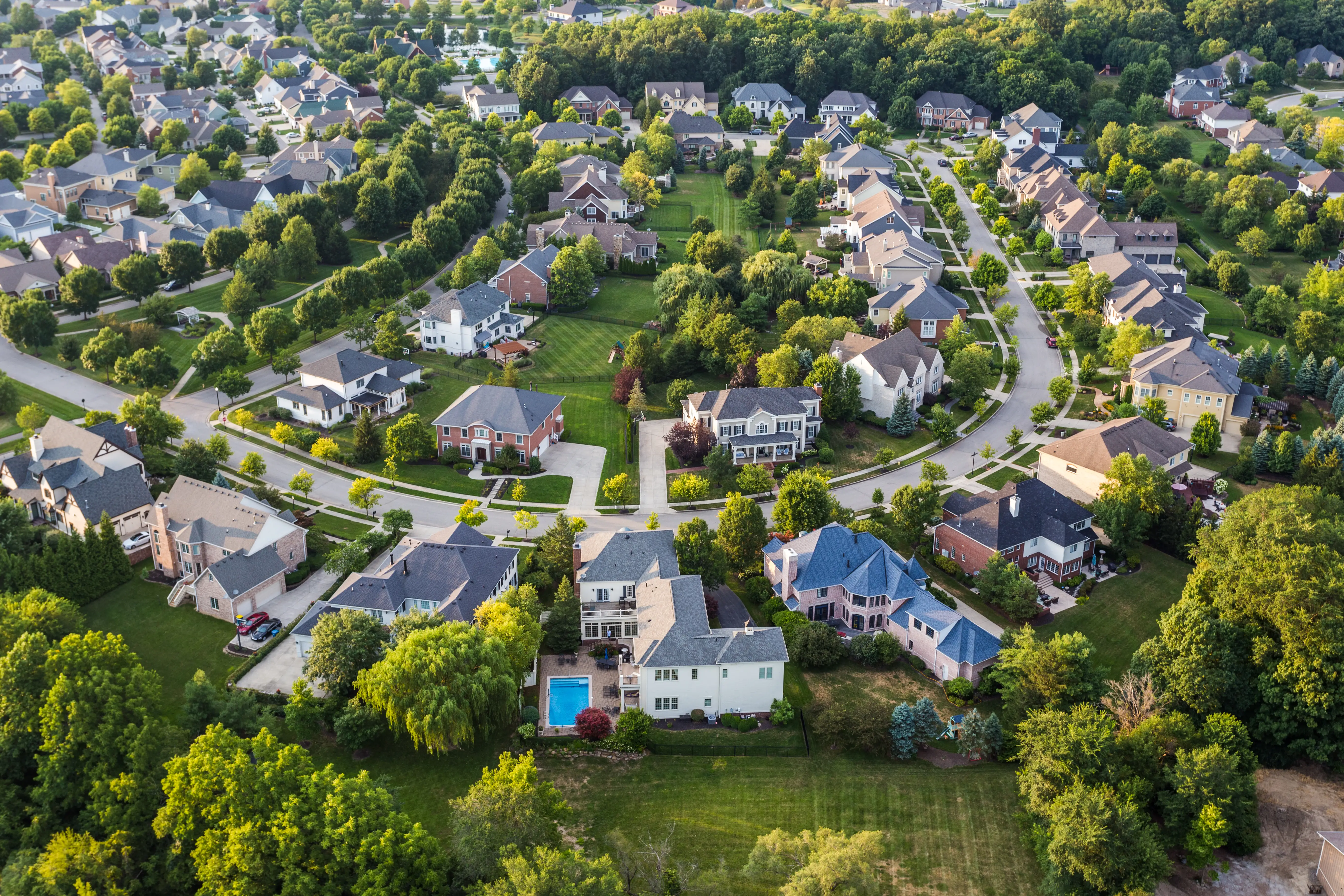 An aerial view of a neighborhood with large homes, including one in the foreground with a pool.