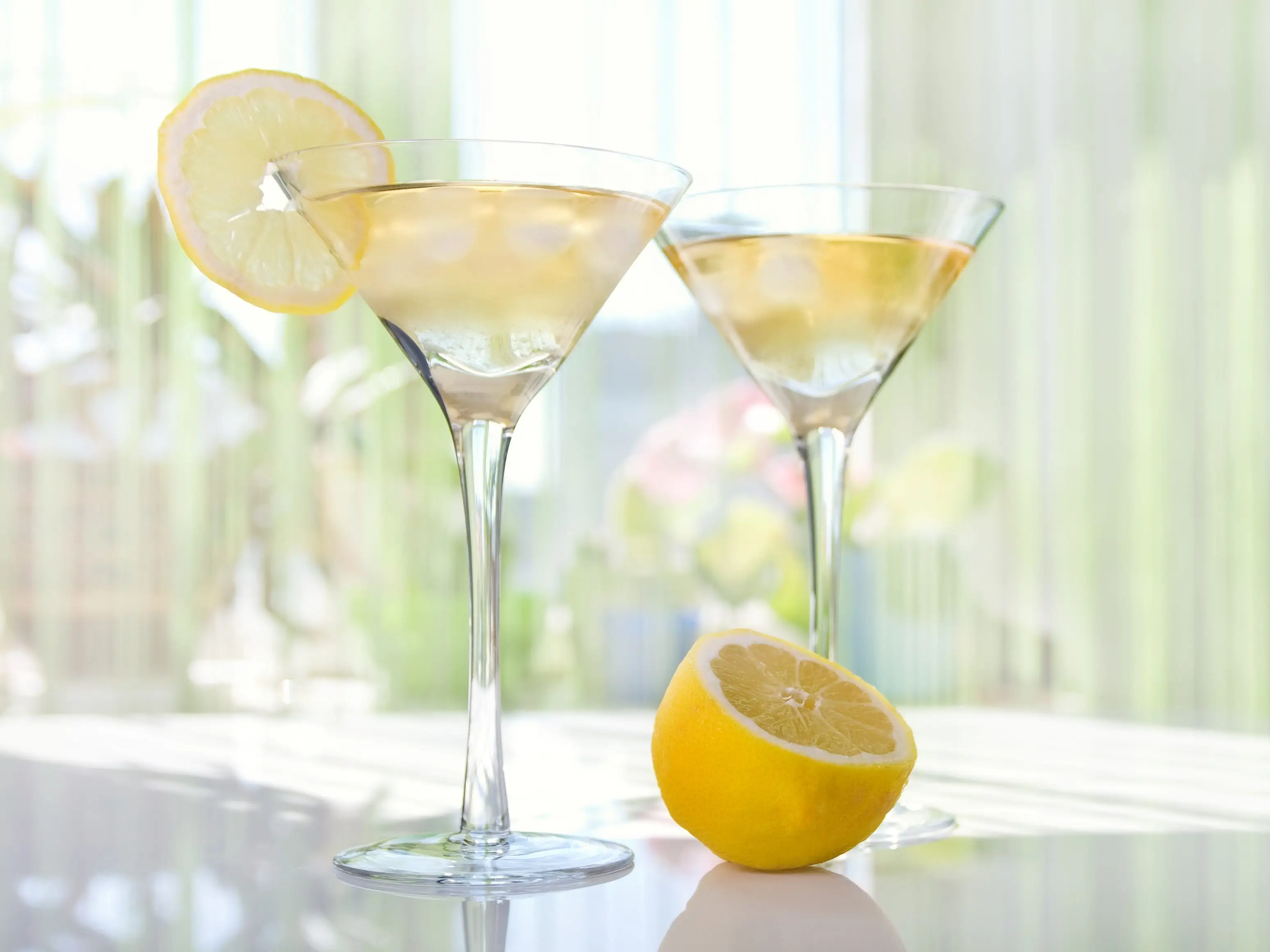 Lemon-drop martinis on a white surface with a lemon slice on the rim of one of the glasses.