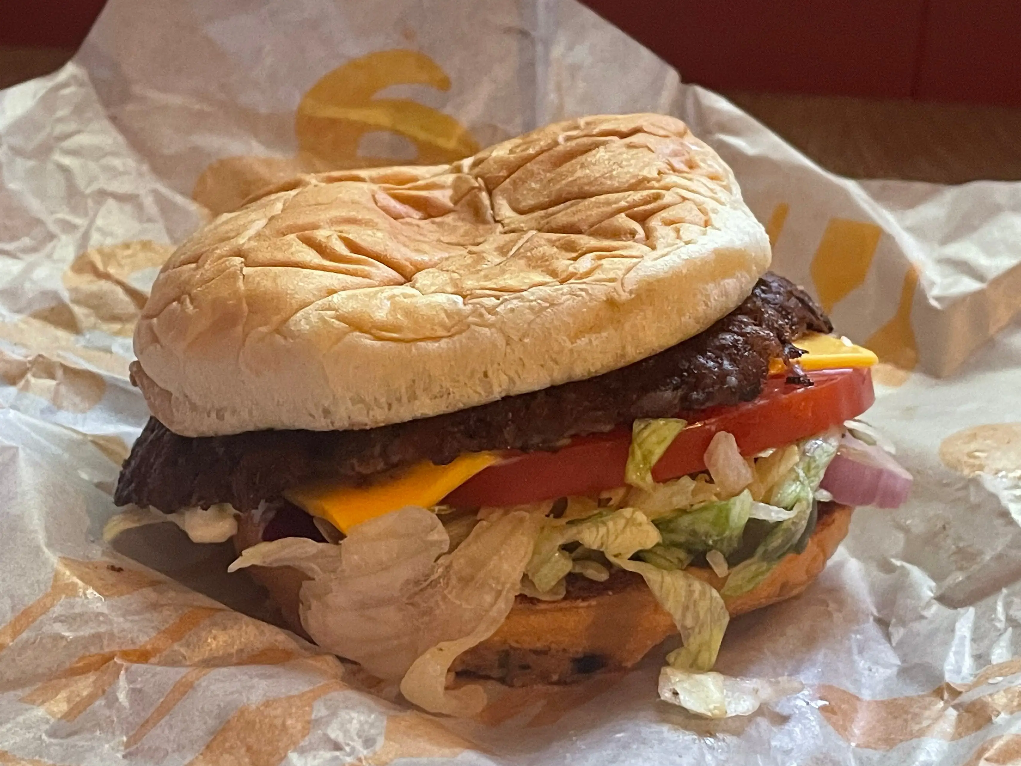 A cheese burger on yellow and white wrapping.