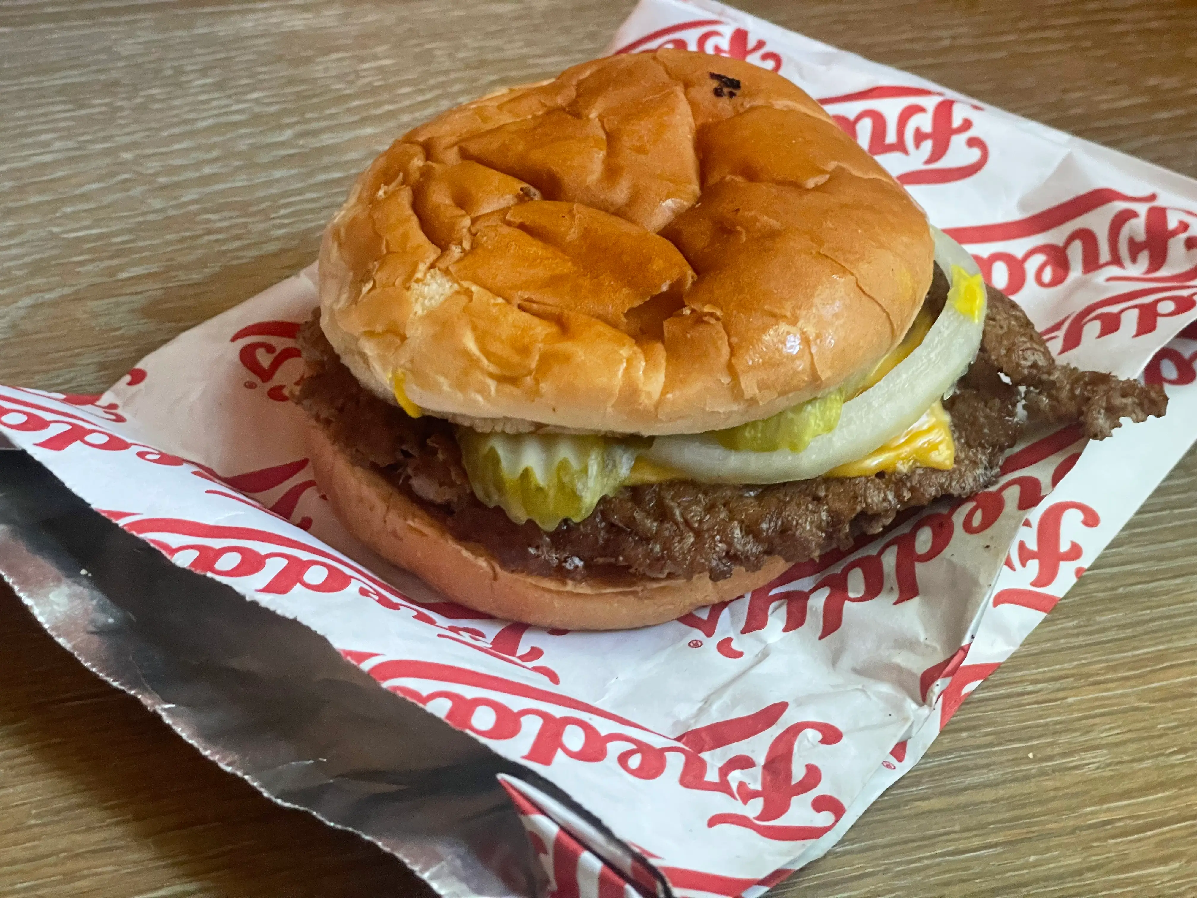 A cheese burger on top of a Freddy's paper bag.