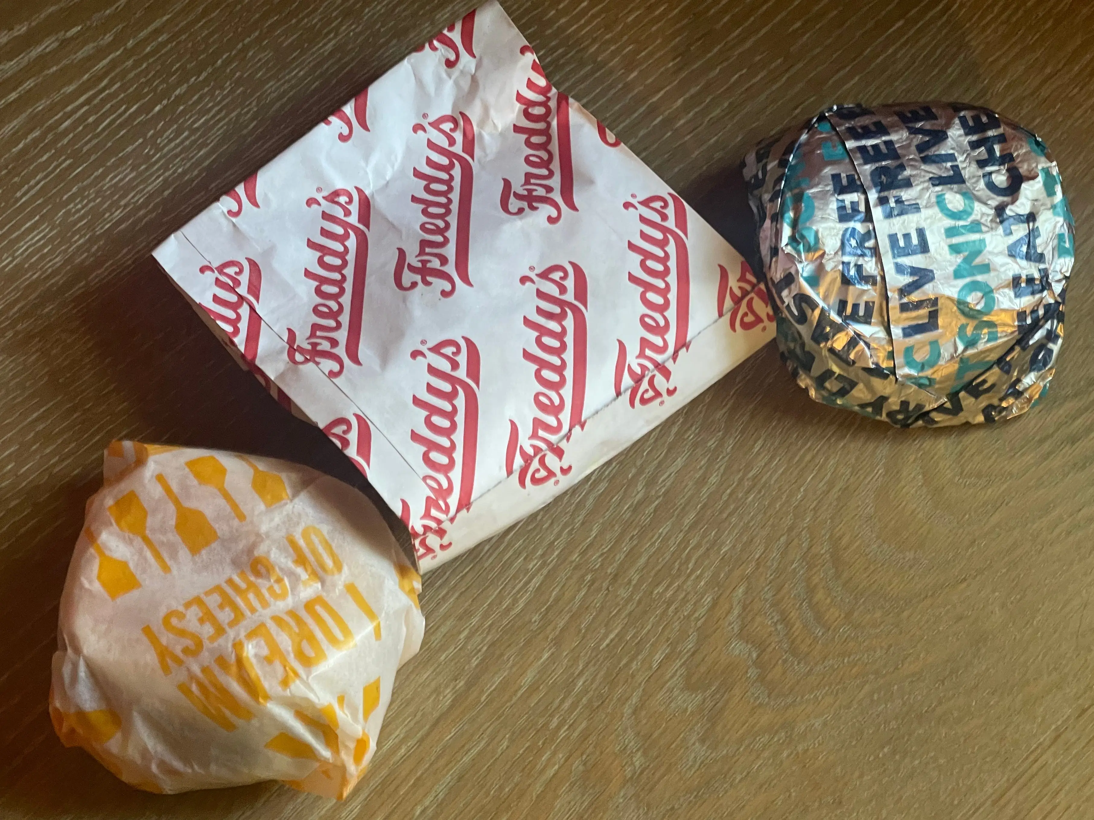 Three wrapped burgers from Culver's, Freddy's, and Sonic.