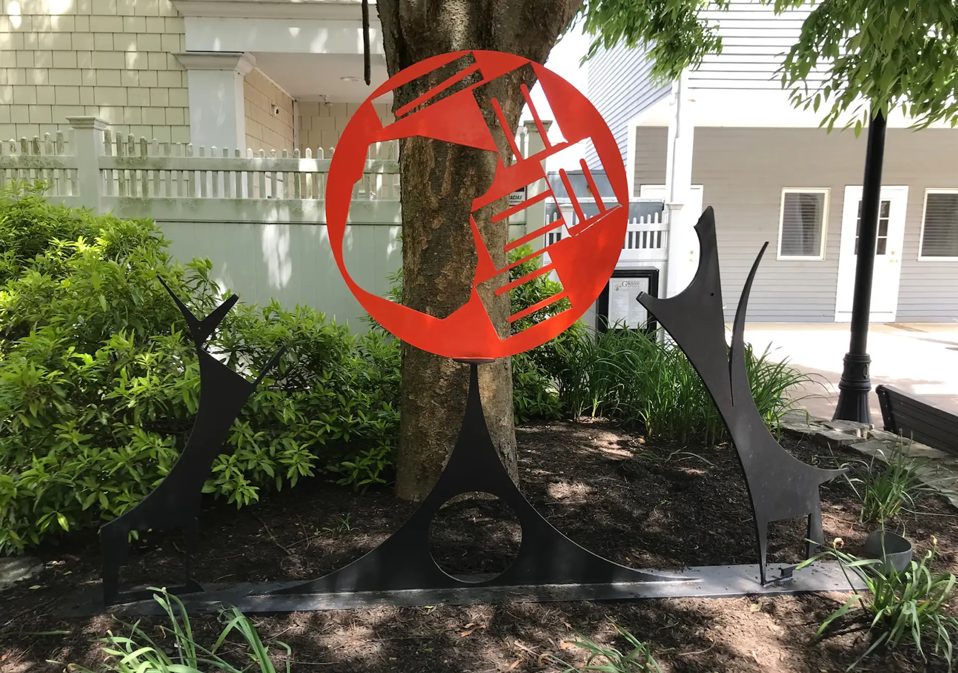 A sculpture with black and red silhouettes in front of a tree.
