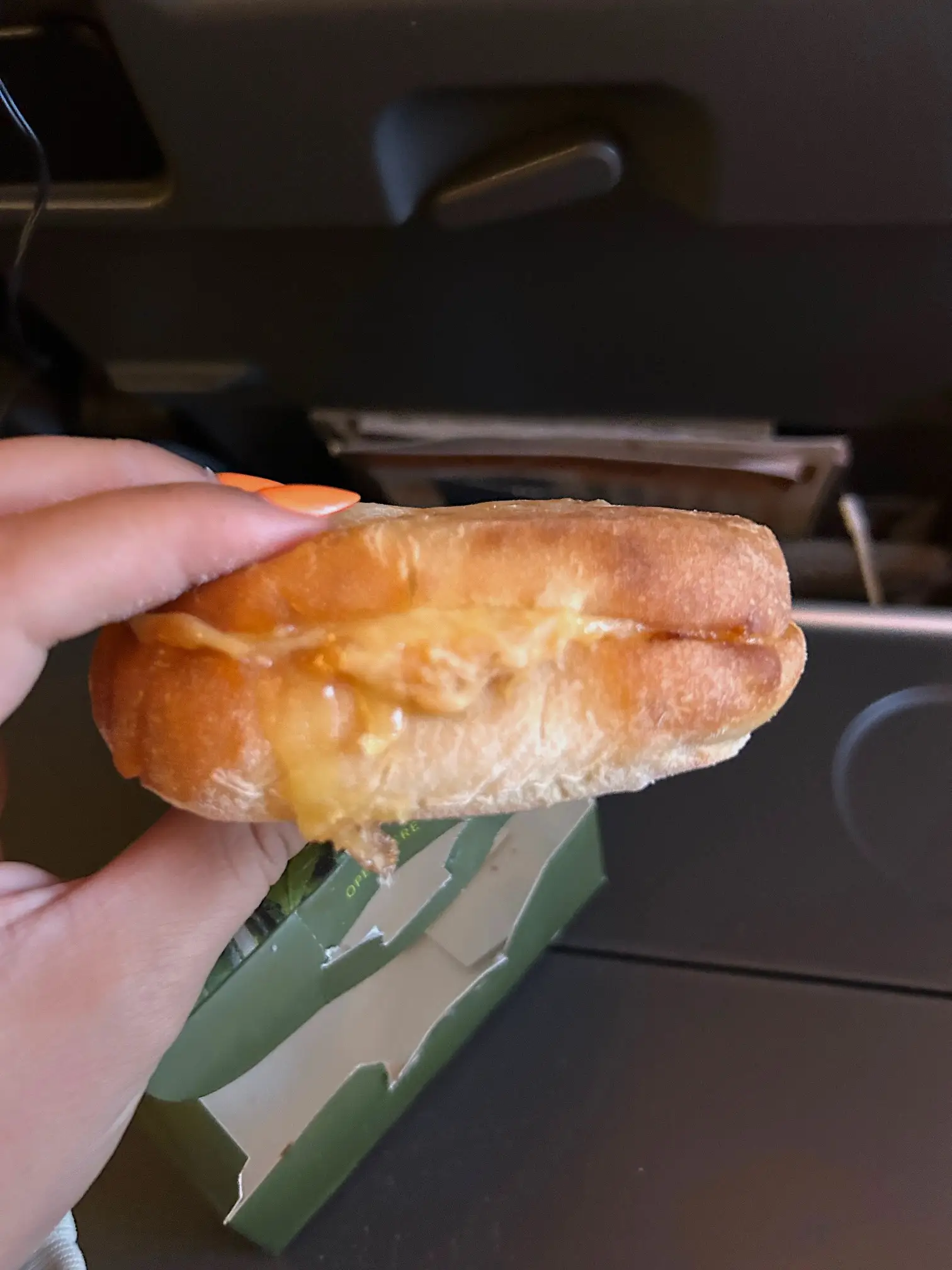 A hand holding a sandwich filled with melted cheese.