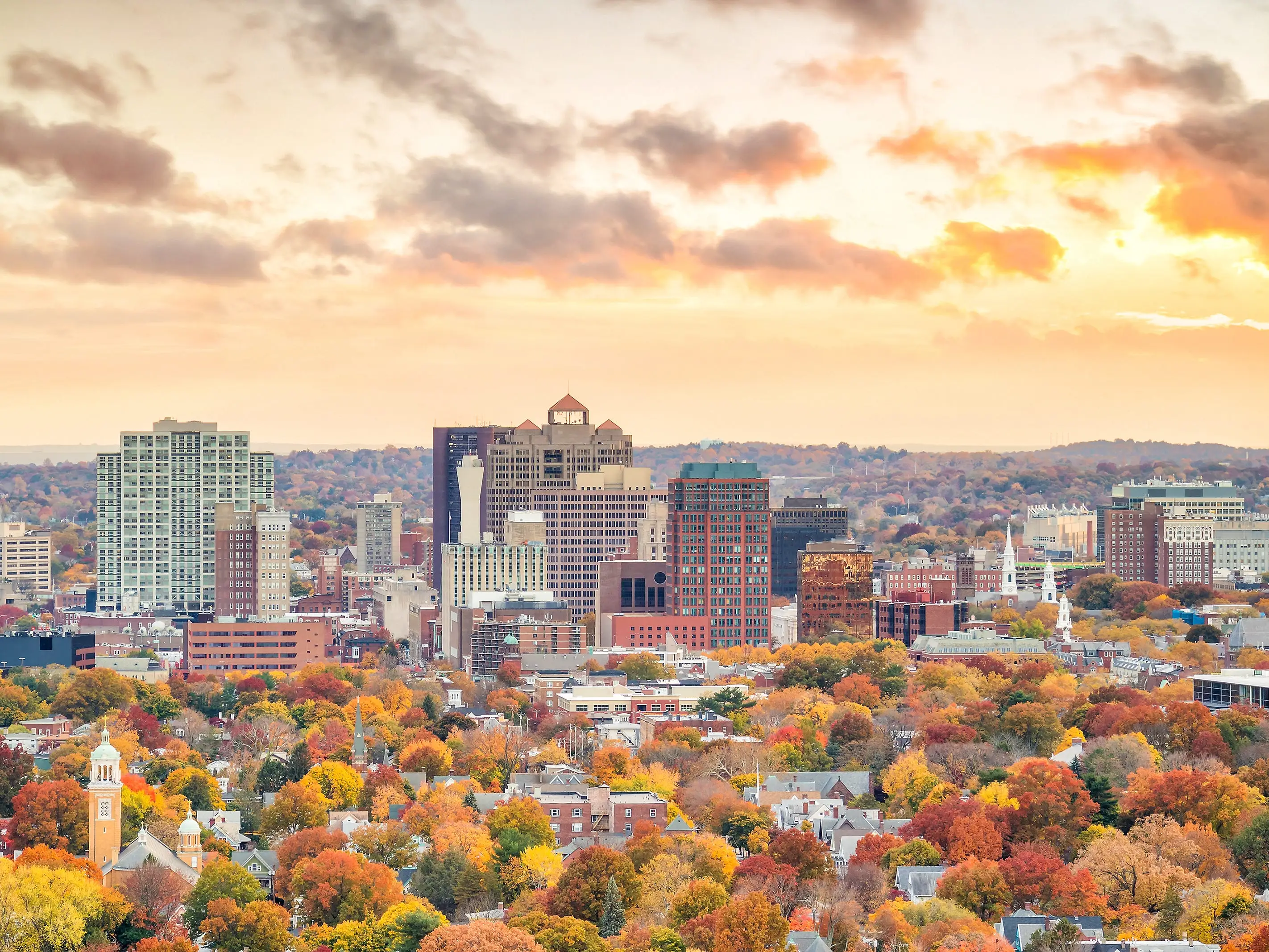 Downtown New Haven, Connecticut, during fall. The trees are varying shades of green, orange, yellow, and red. The sky has an orange tint, too.