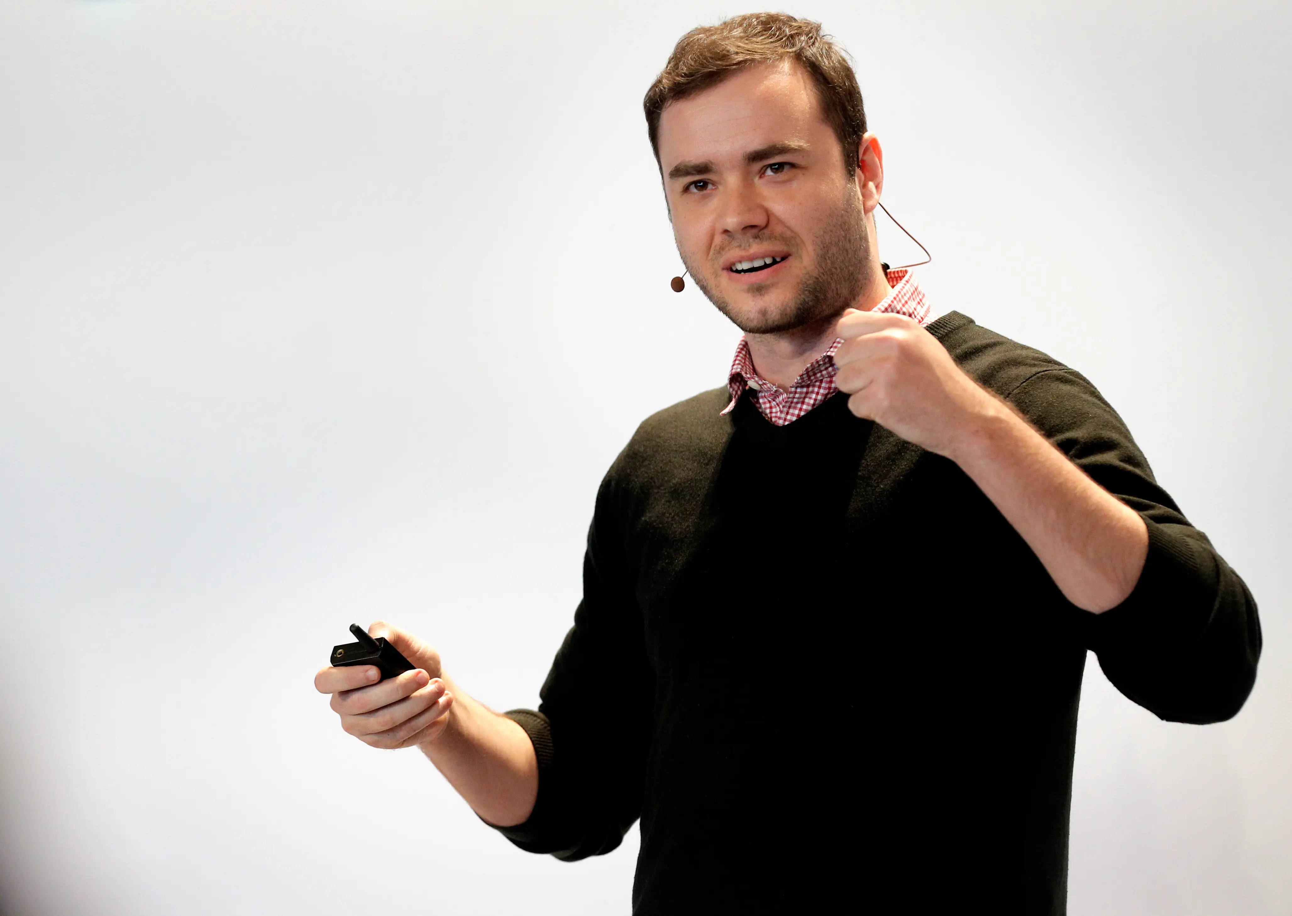 Andrej Karpathy, wearing a black sweater and a button-up shirt, talks onstage in front of a white screen.
