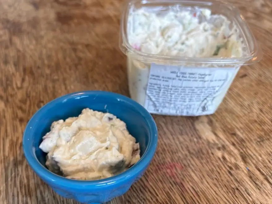 A small blue bowl of Whole Foods Red Bliss potato salad next to the container.