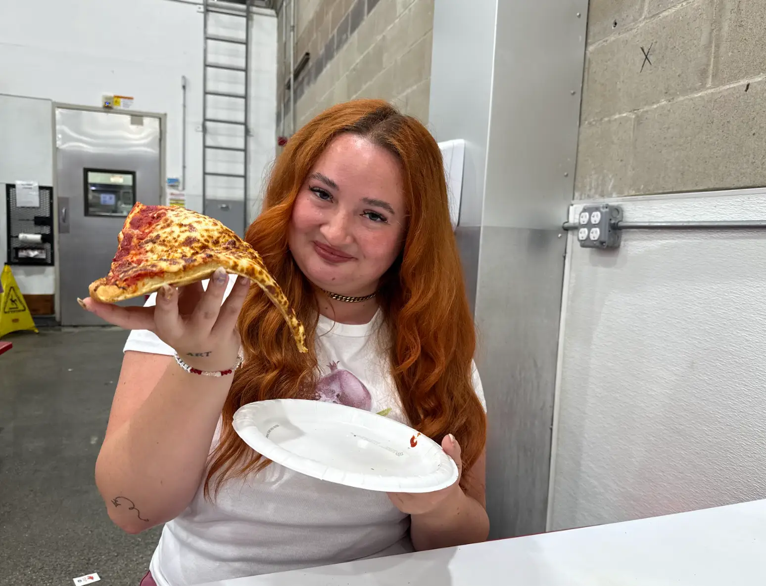 The writer holding a slice of pizza from Costco.