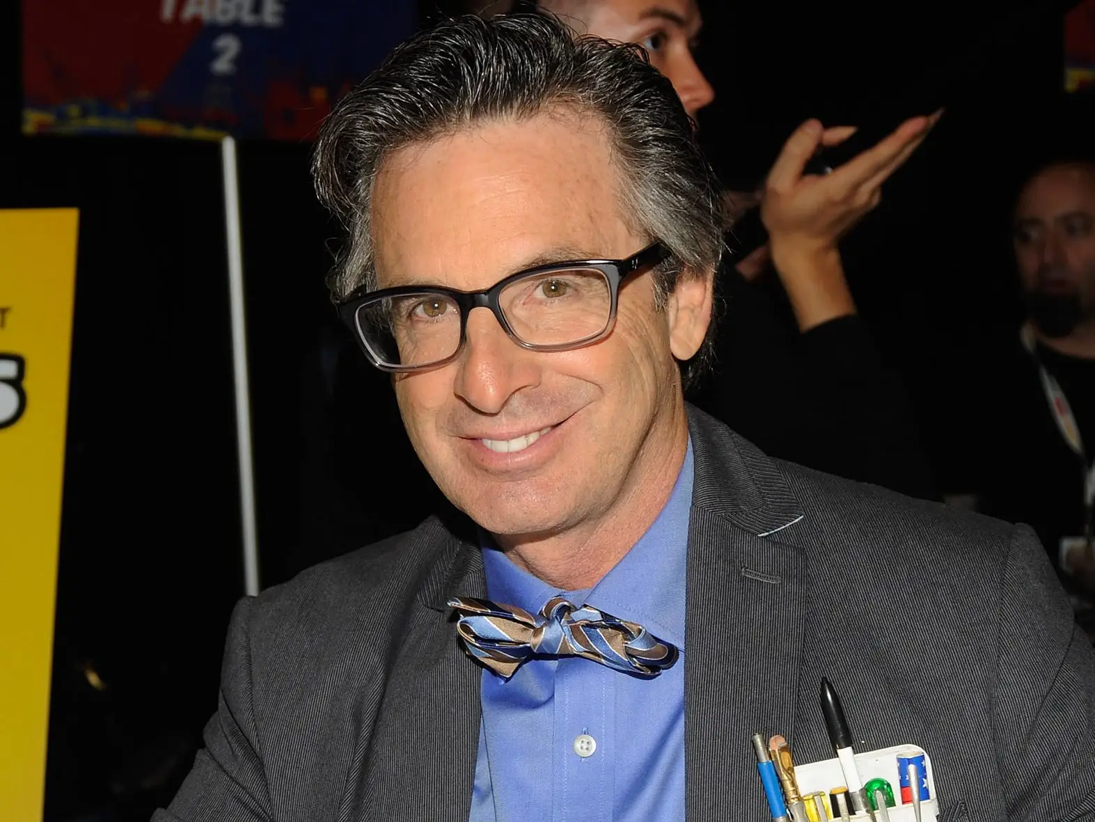 Robert Carradine in a grey suit with a bow tie and pocket protector filled with pens