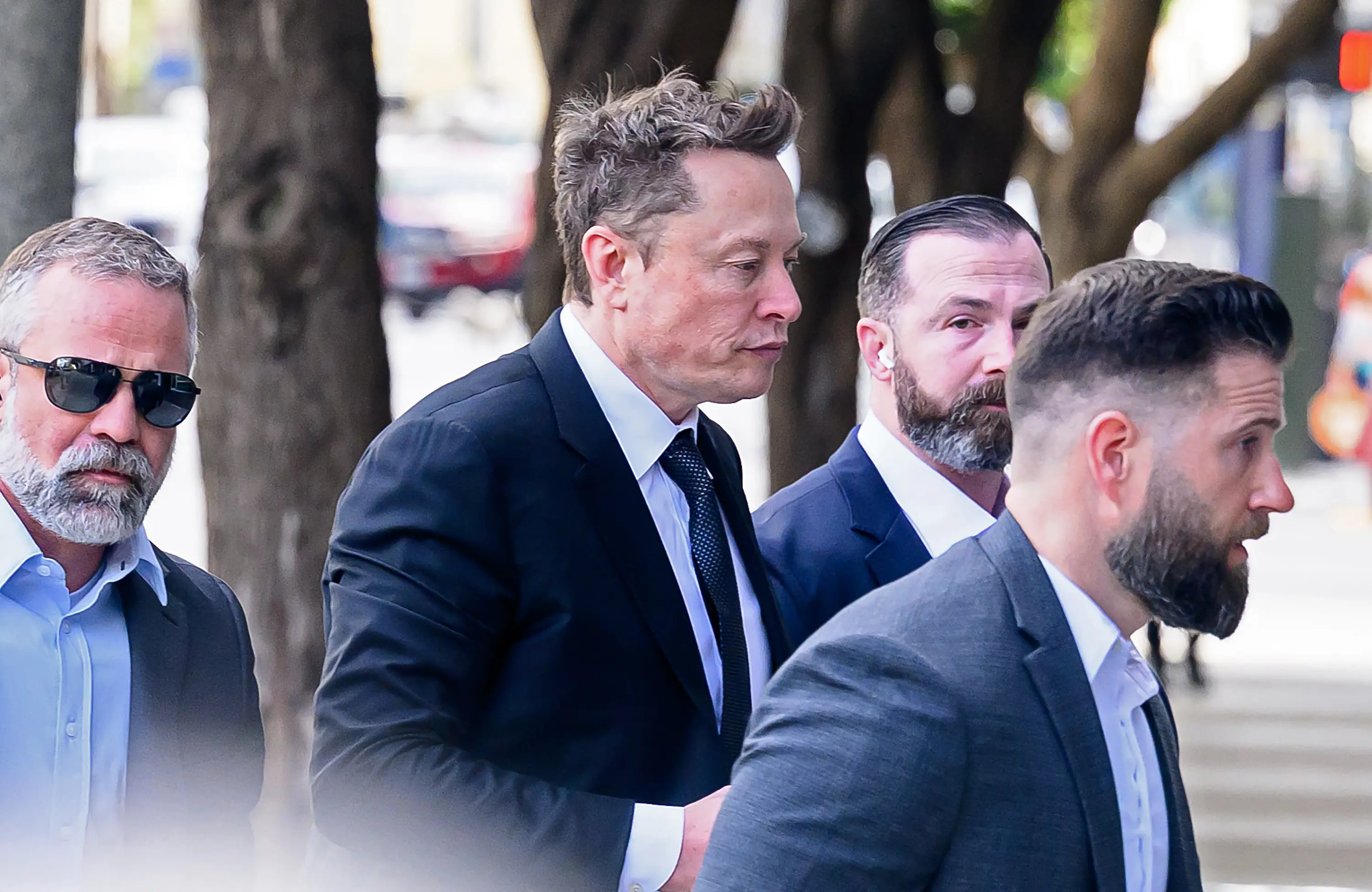 Elon Musk arrives at federal court with three security personnel surrounding him.