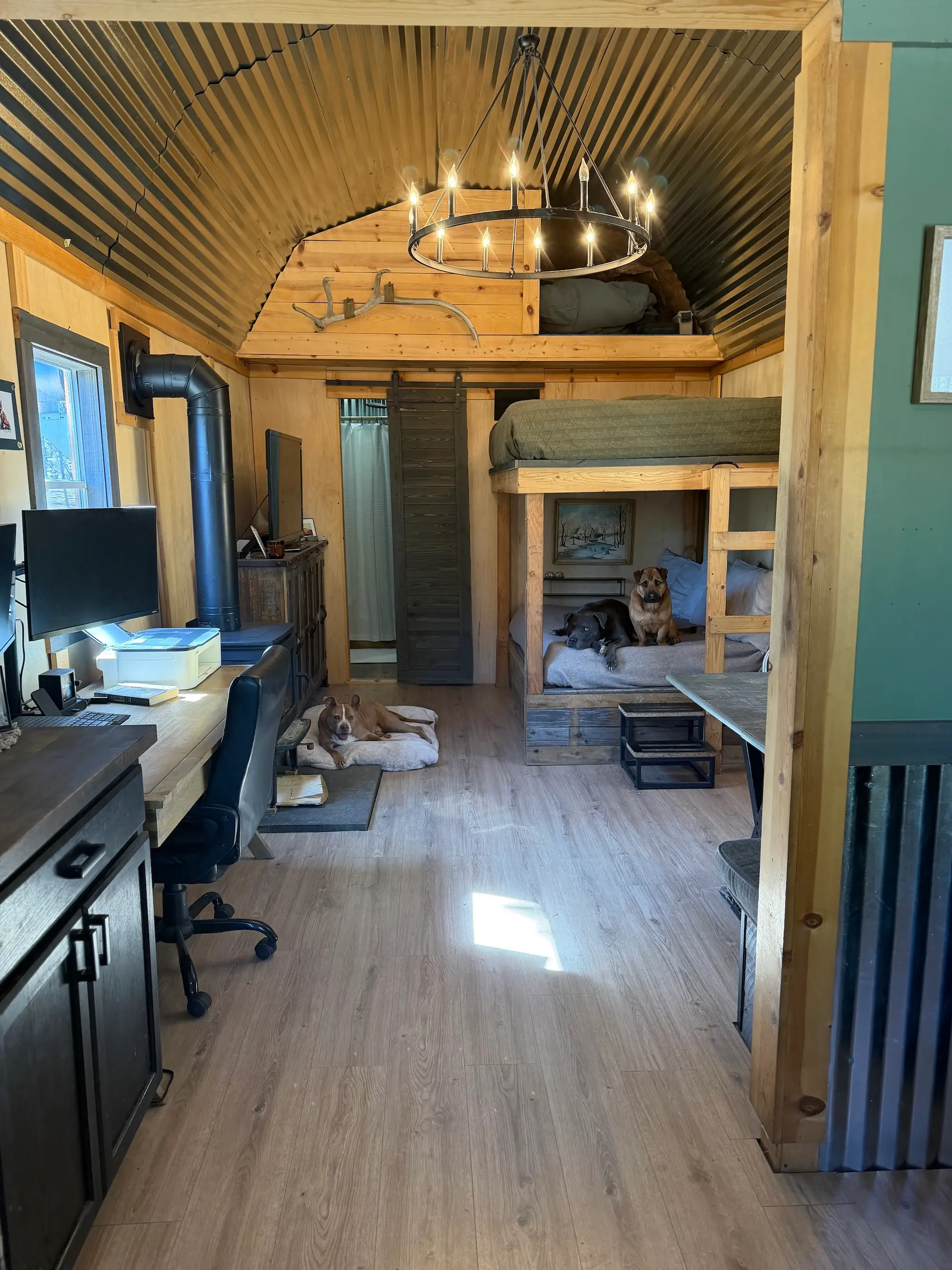 A tiny home with a wood stove, desk, and a bunk bed.