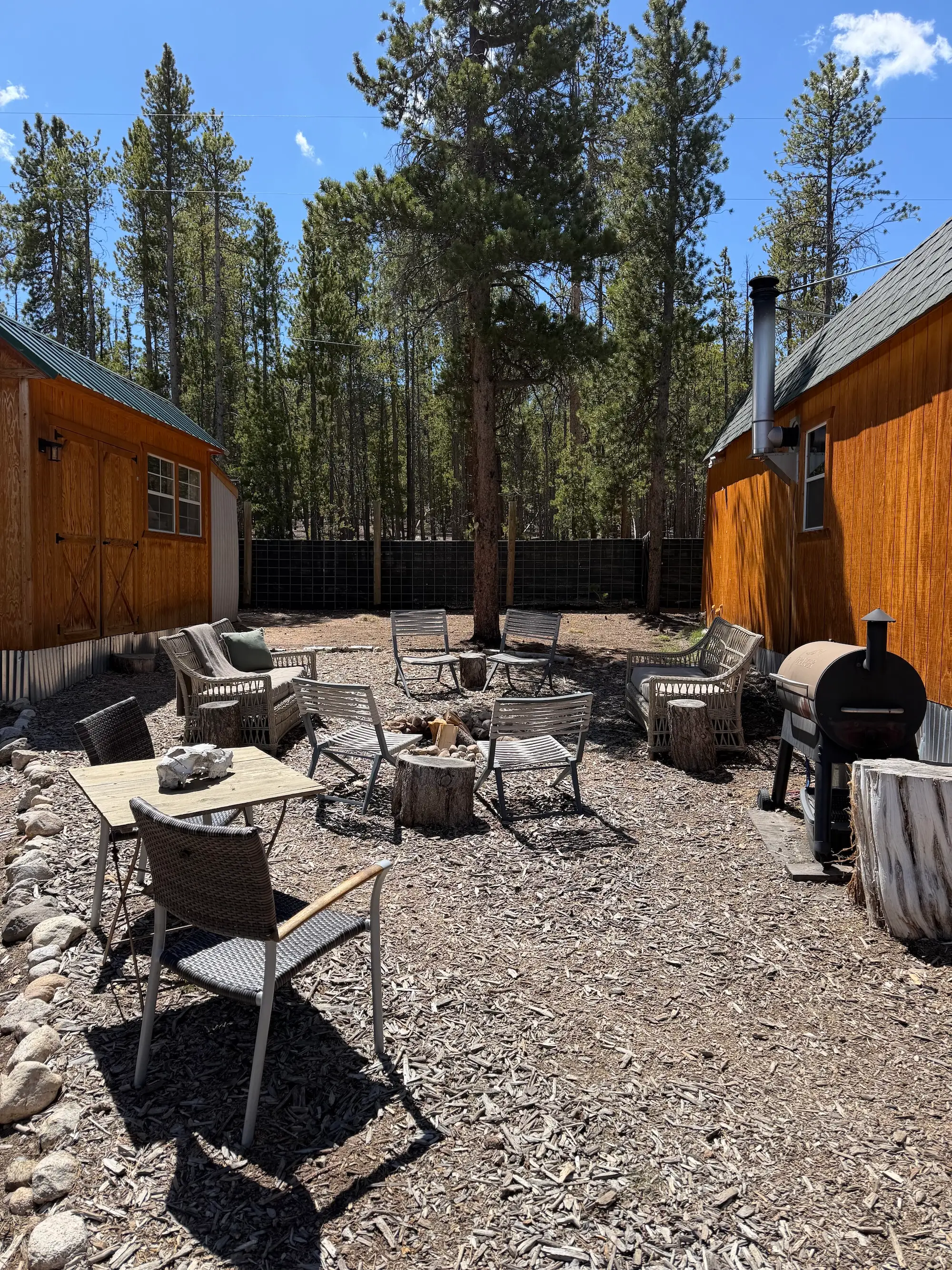 A firepit surrounded by chairs between two sheds.
