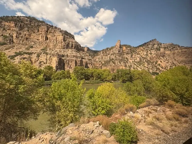 The view of mountains along a river out the window of a train.