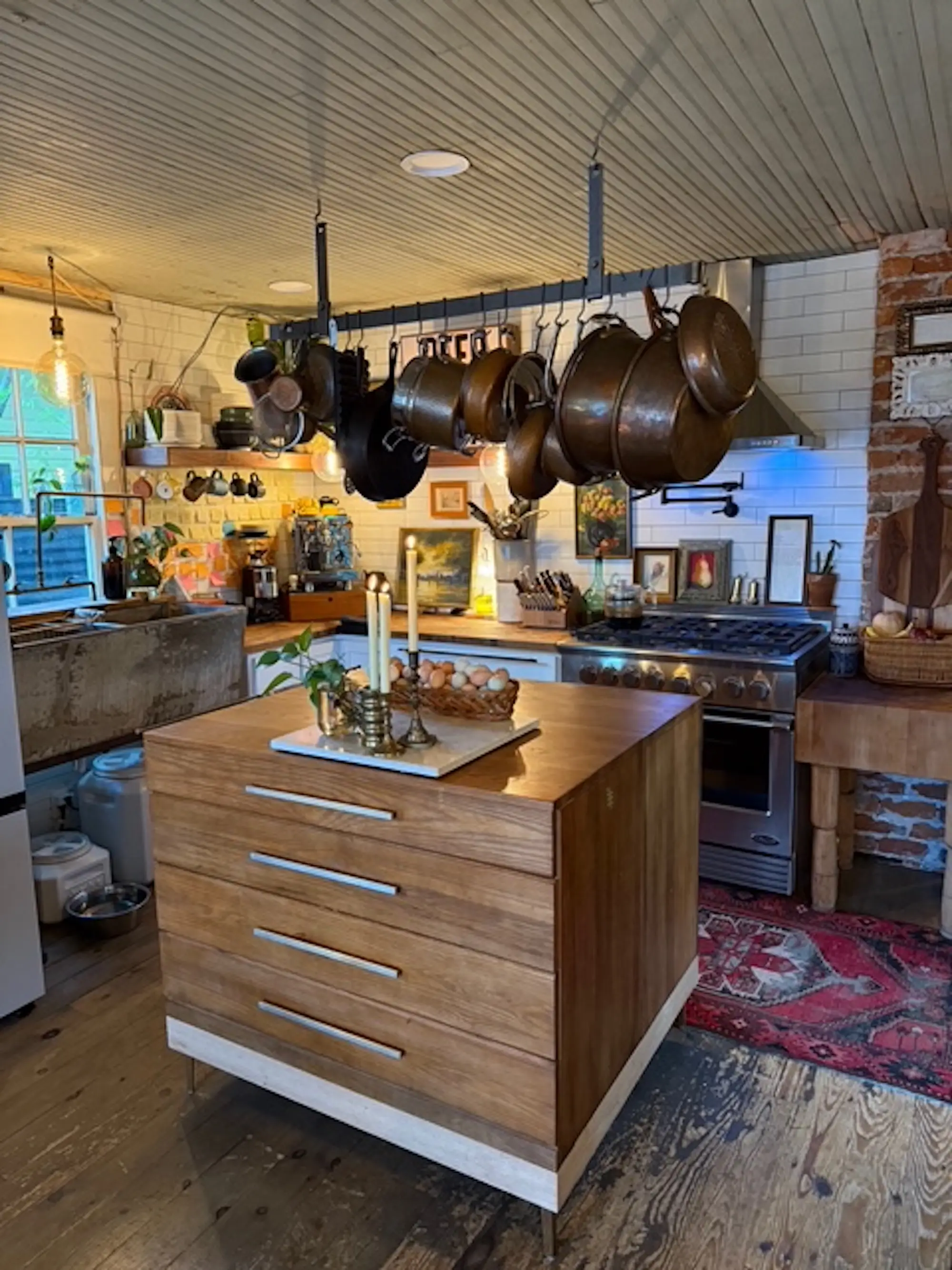 A kitchen with a large island and hanging pots and pans.