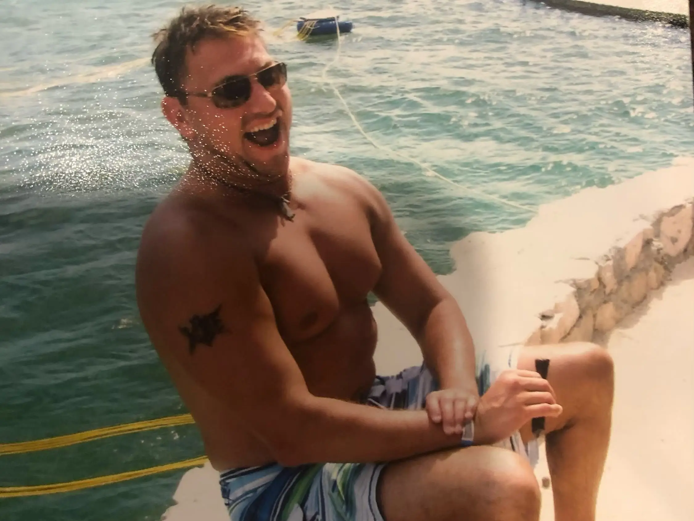 A bare-chested man sitting on the side of a swimming pool.