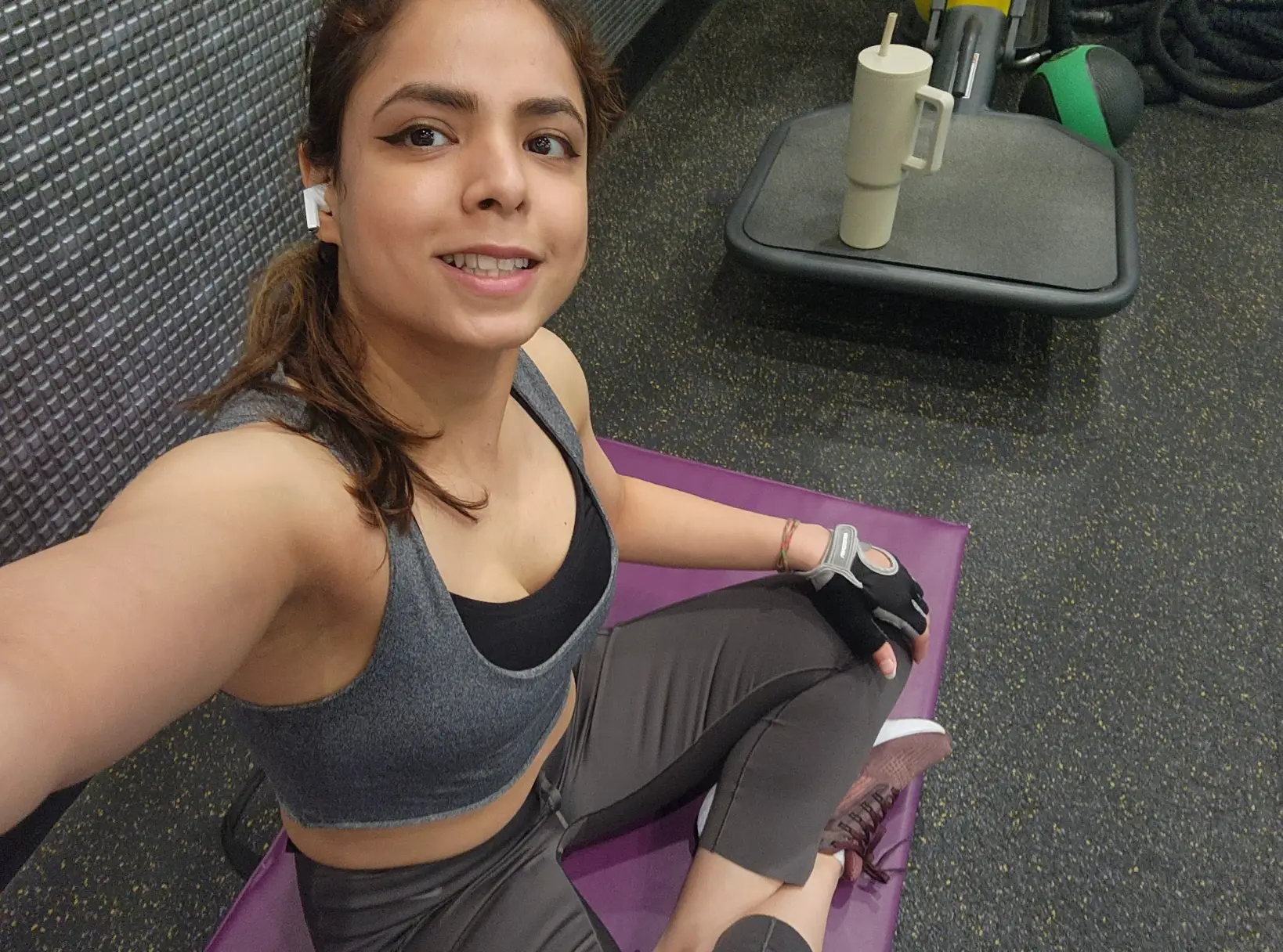 The writer posing on a purple mat, wearing AirPods and workout gear.