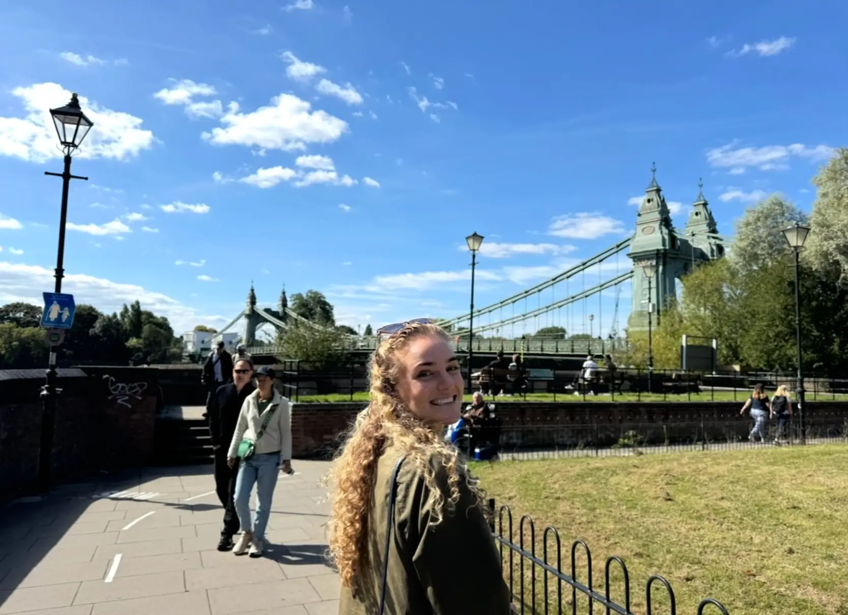 The writer posing in front of a green lawn and bridge in the UK.