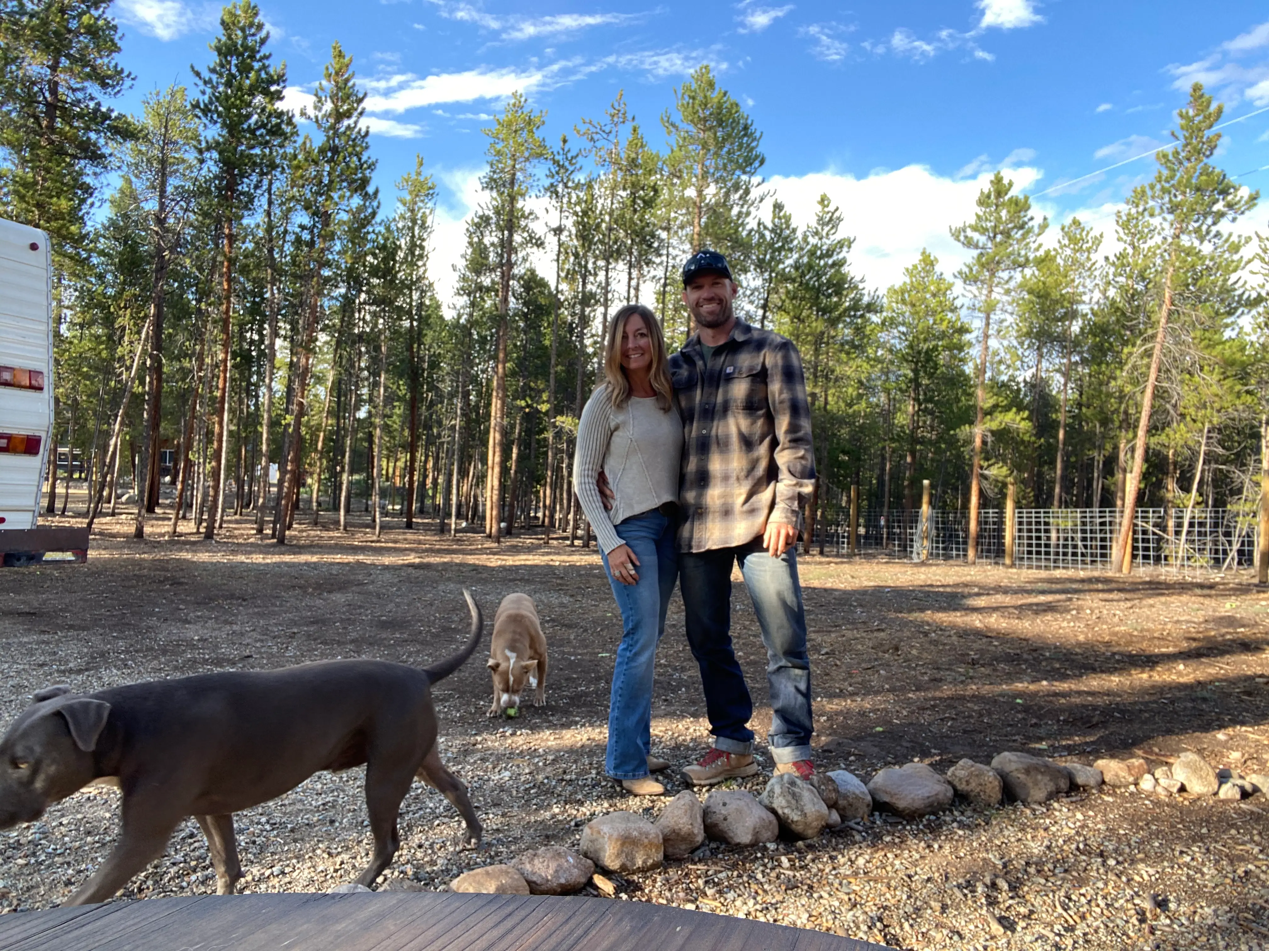 A couple stands in a wooded area with two dogs.