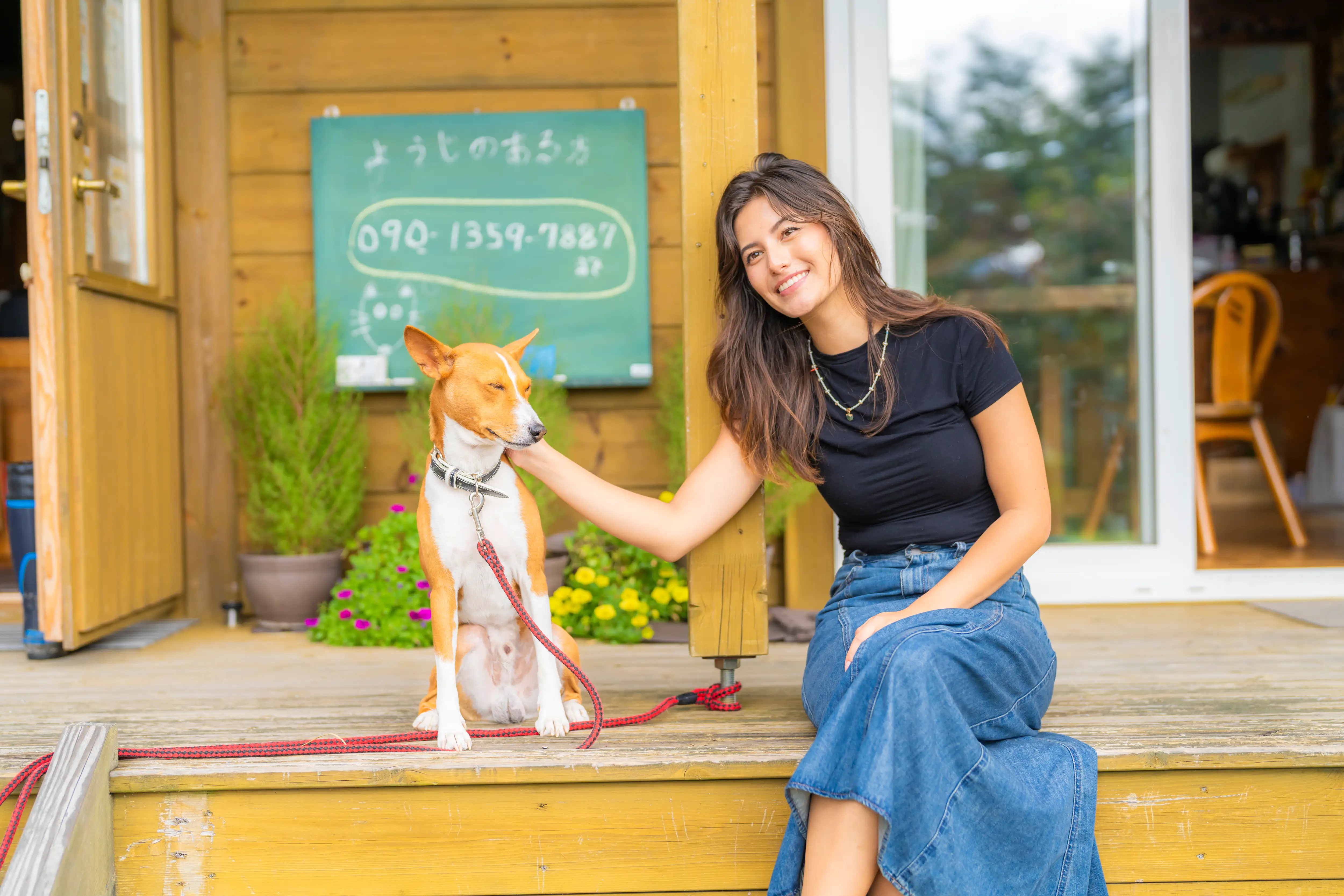 A woman sitting with a dog on the step of an outdoor porch in Japan.