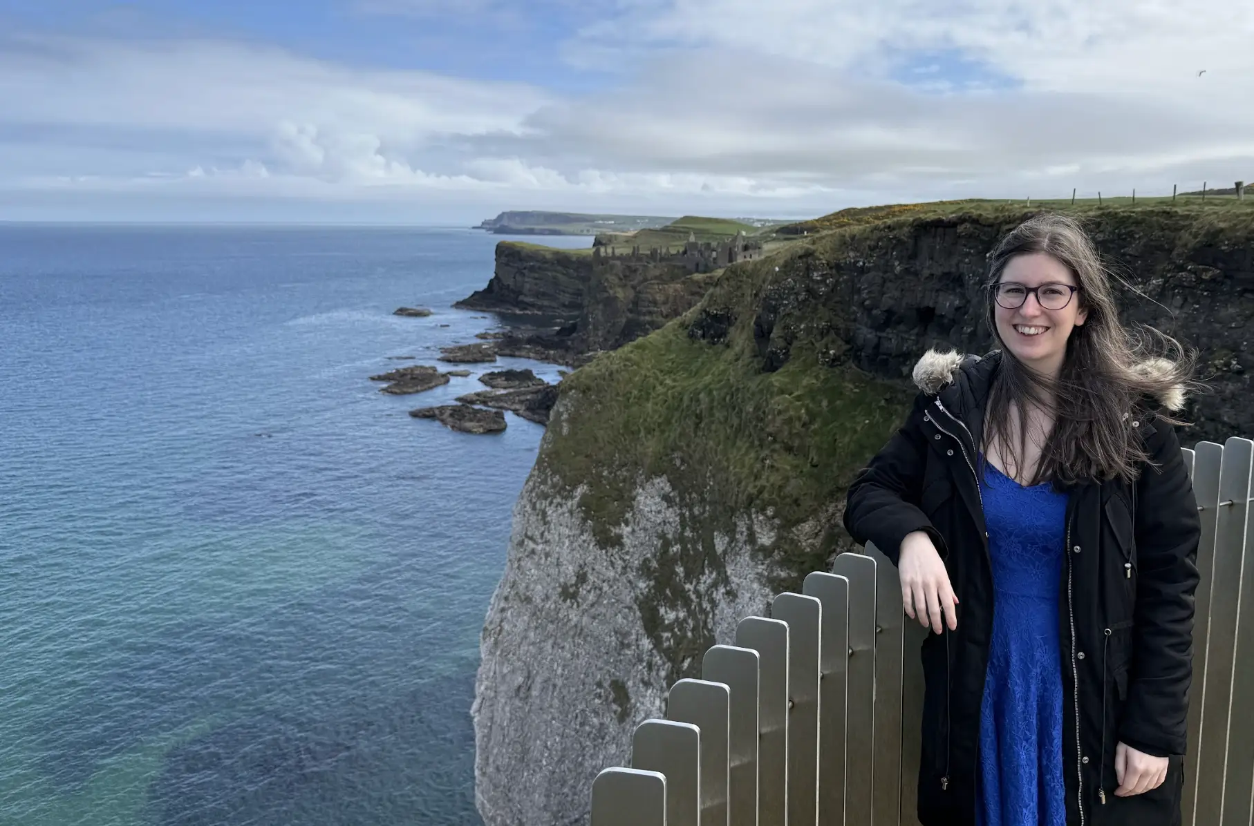 The writer standing in front of the Dunluce Castle ruins with a view of the water in Northern Ireland.