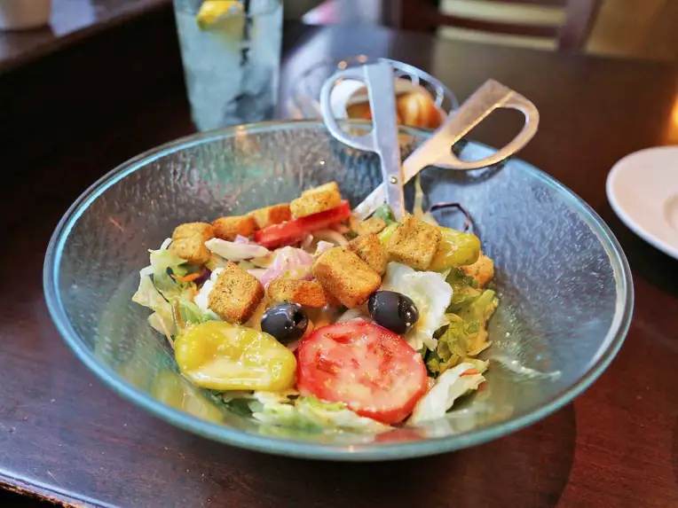 Salad at Olive Garden with croutons, olives, tomato, tongs in bowl
