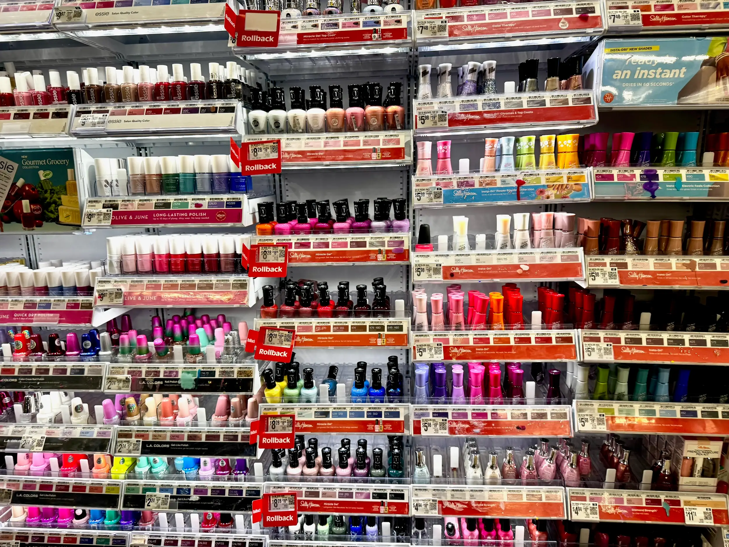 Rows of colorful nail polish bottles line store shelves with rollback signs and paper price tags.