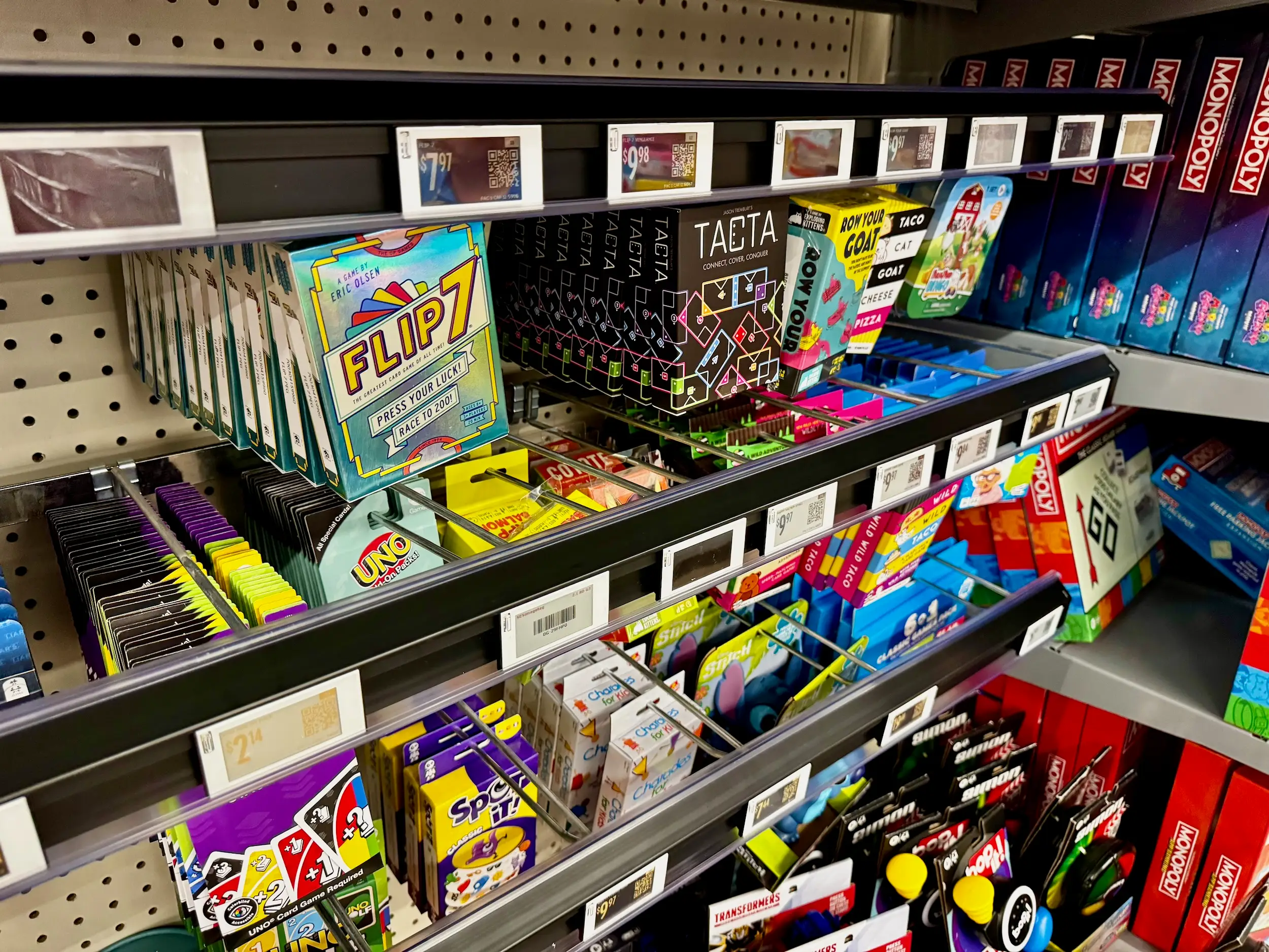 A store shelf displays various board games and card games with electronic price tags along the edge.