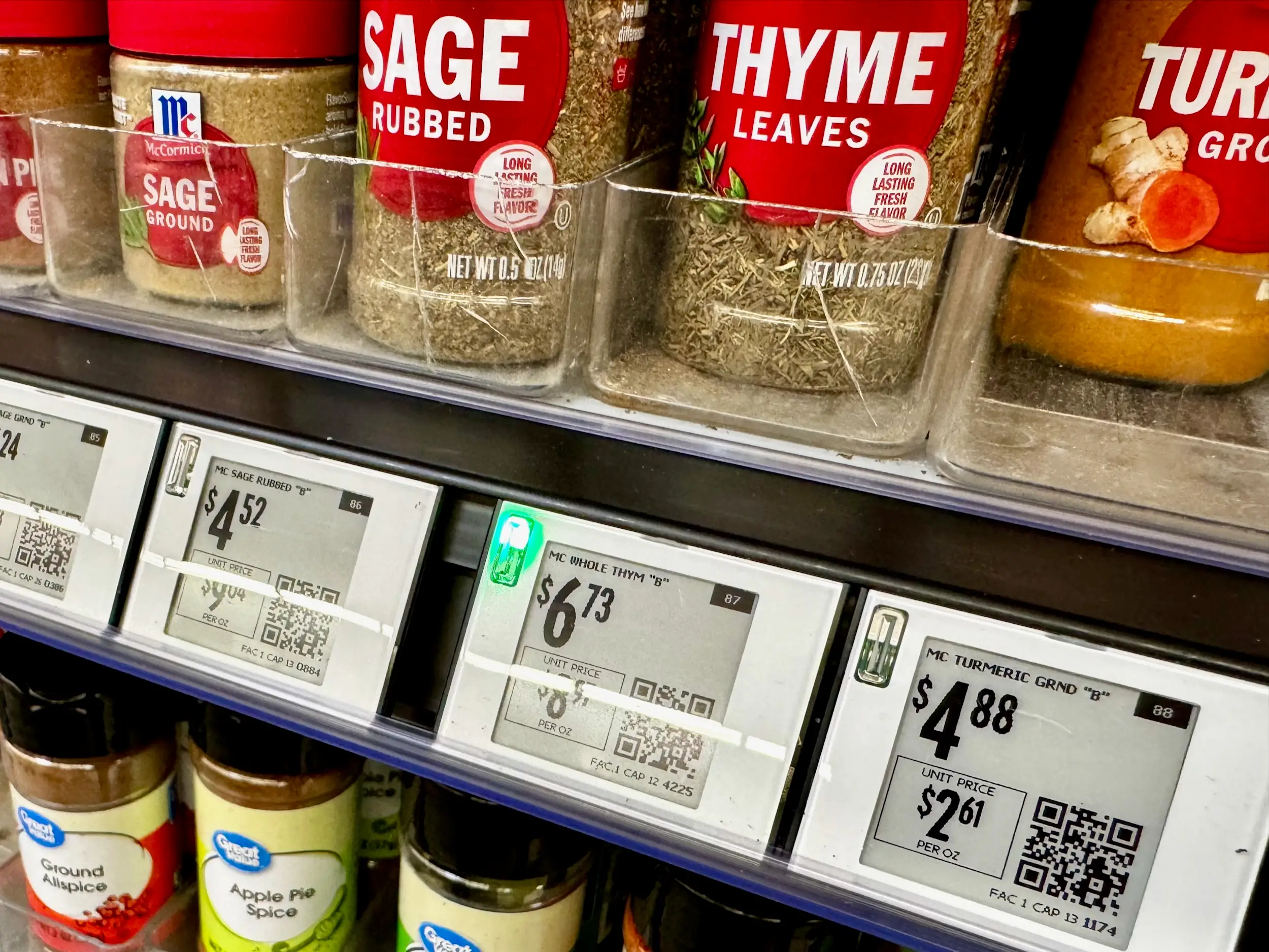 Jars of spices including sage and thyme are displayed with electronic shelf labels showing prices and QR codes.