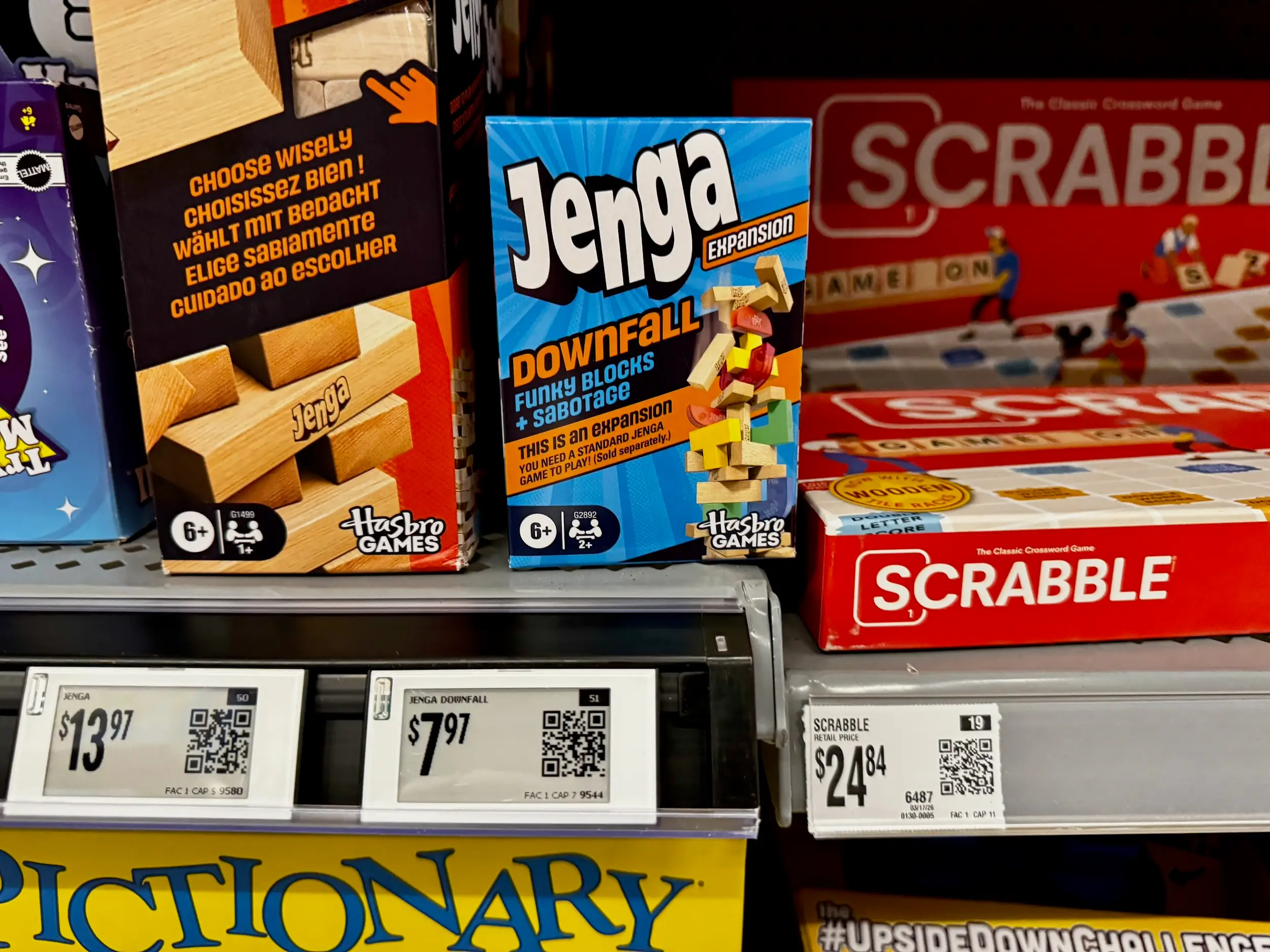 Board games including Jenga and Scrabble sit on a shelf with digital price tags and a paper tag below.
