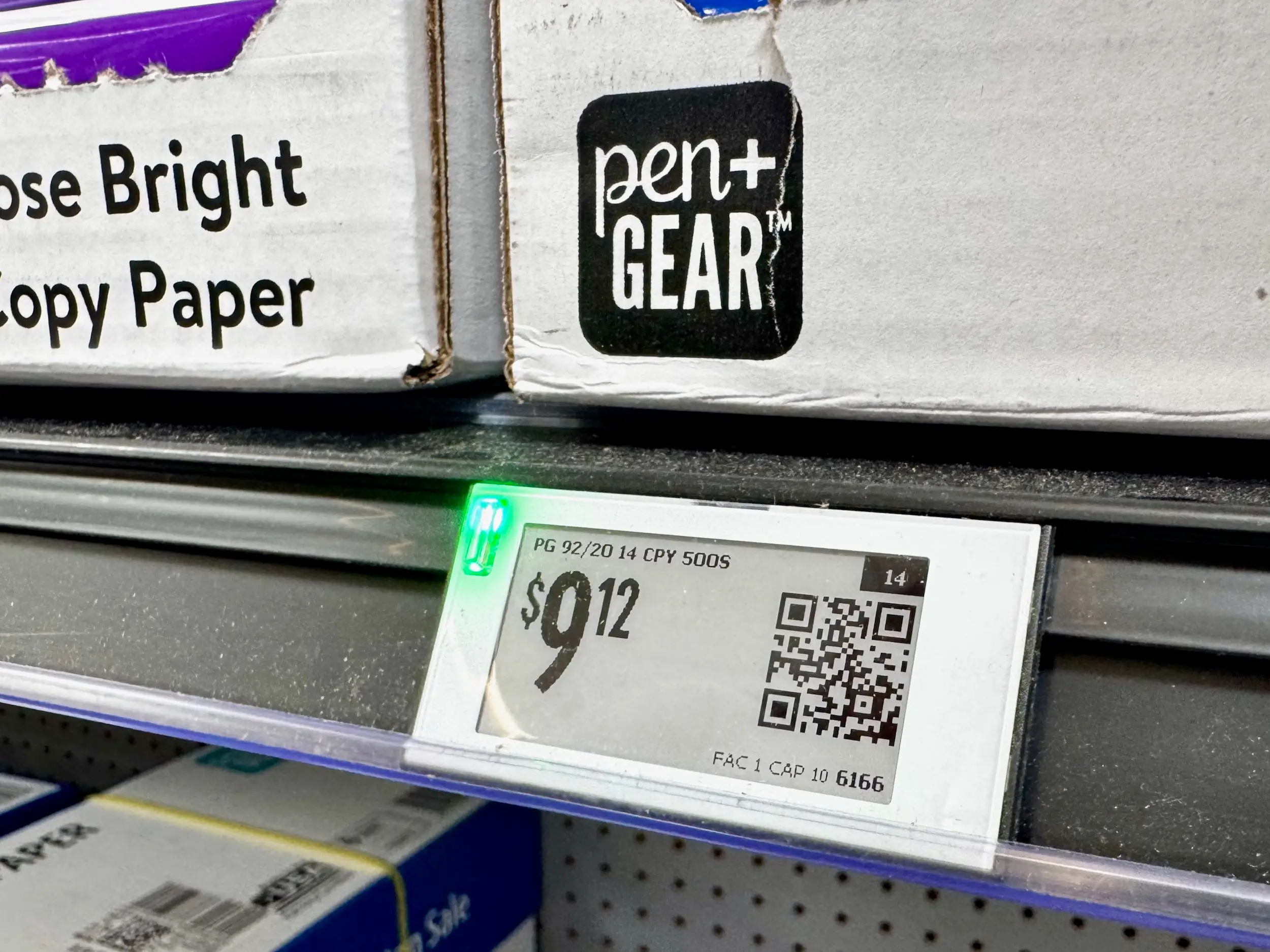 A shelf of copy paper boxes features an electronic price tag.