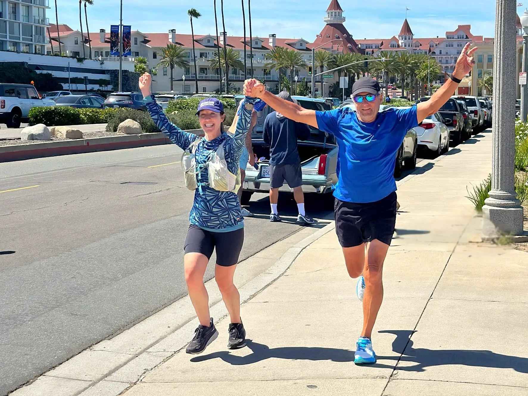 A man running on the street outside with an exercise buddy. The pair is holding hands and raising their arms over their heads in triumph.