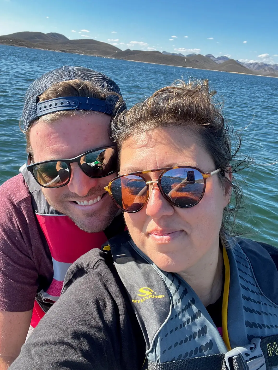 A selfie of a couple in the ocean with mountains behind them.