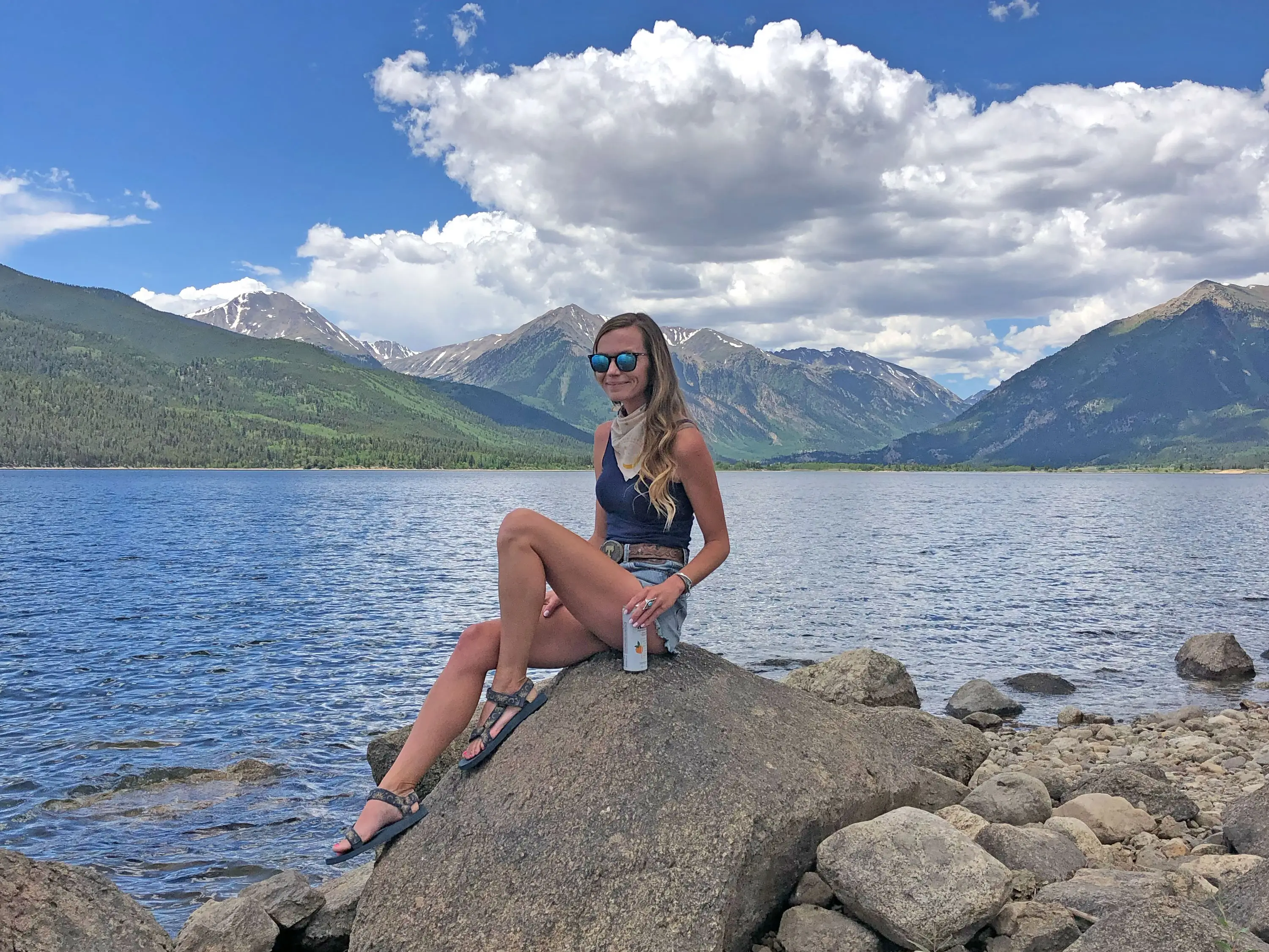 Emily sits on a rock near a lake with mountains in the background.