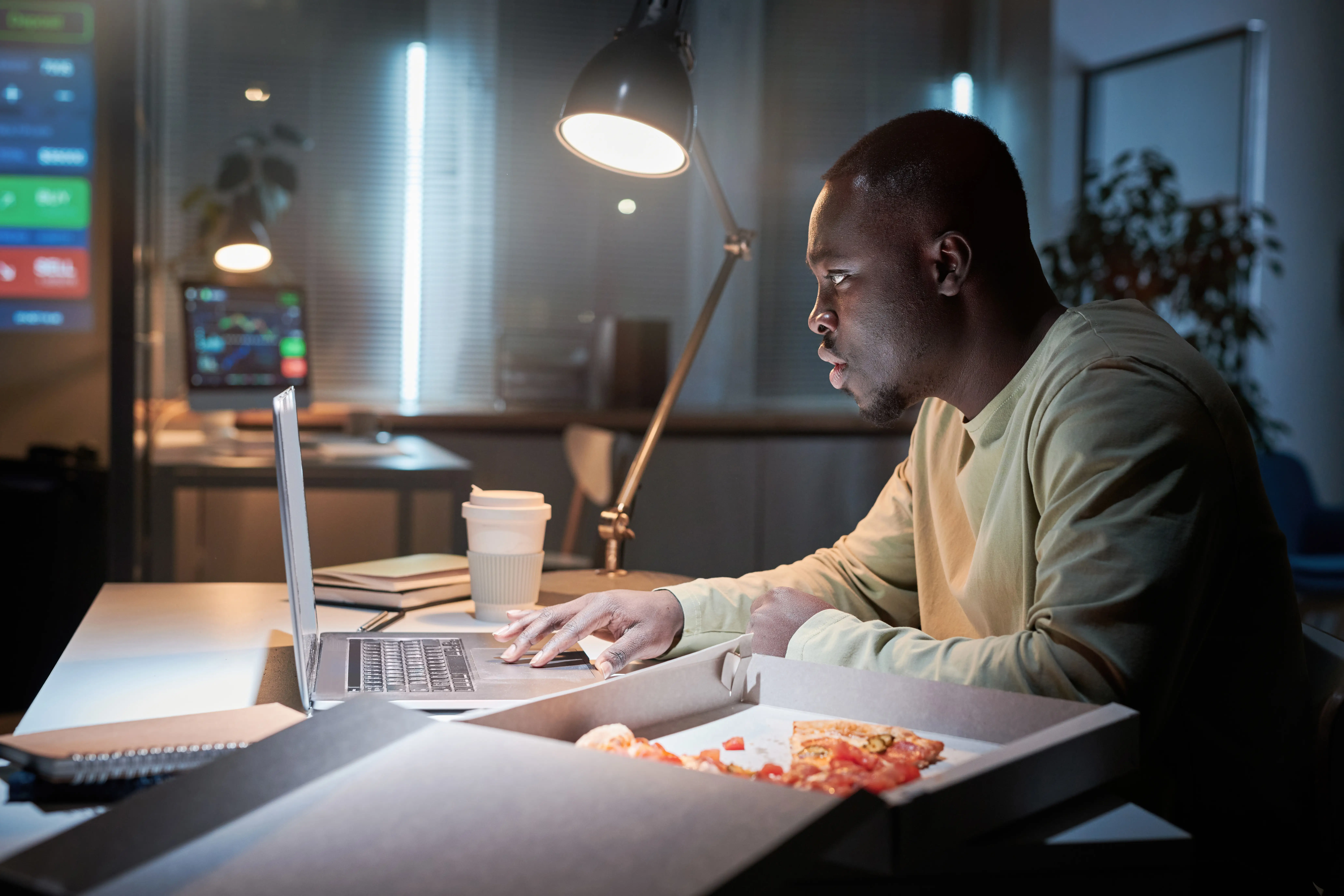 Man eating pizza at an office late at night.